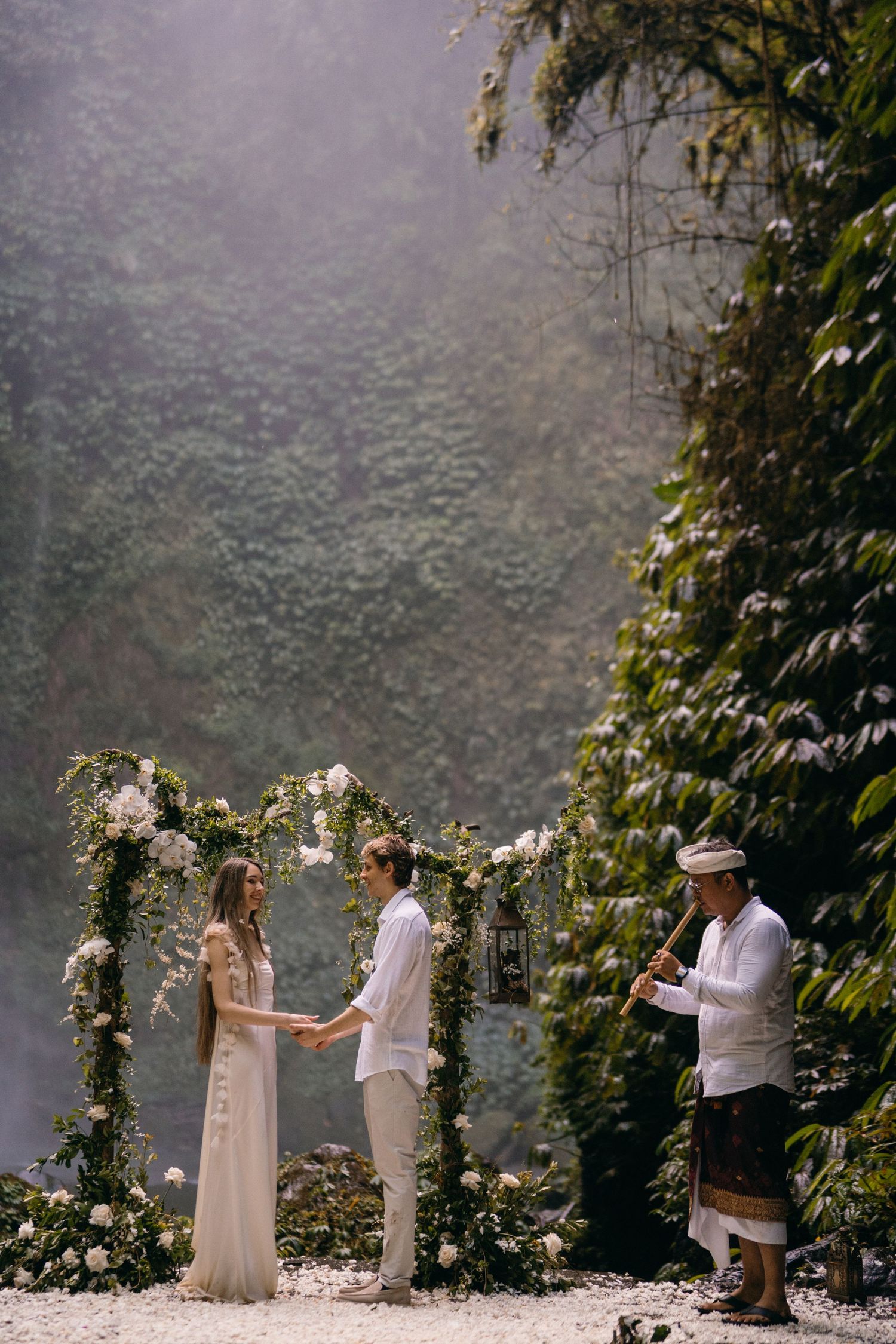 A couple exchanges vows during an intimate garden wedding ceremony surrounded by climbing roses and misty atmosphere.