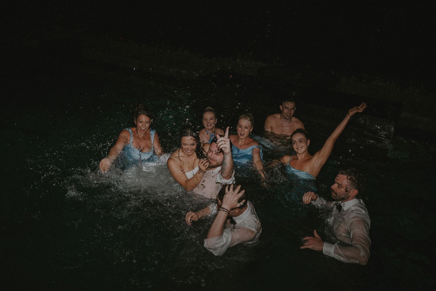 A group of people splash and play in dark water at night during a fun outdoor swimming session.
