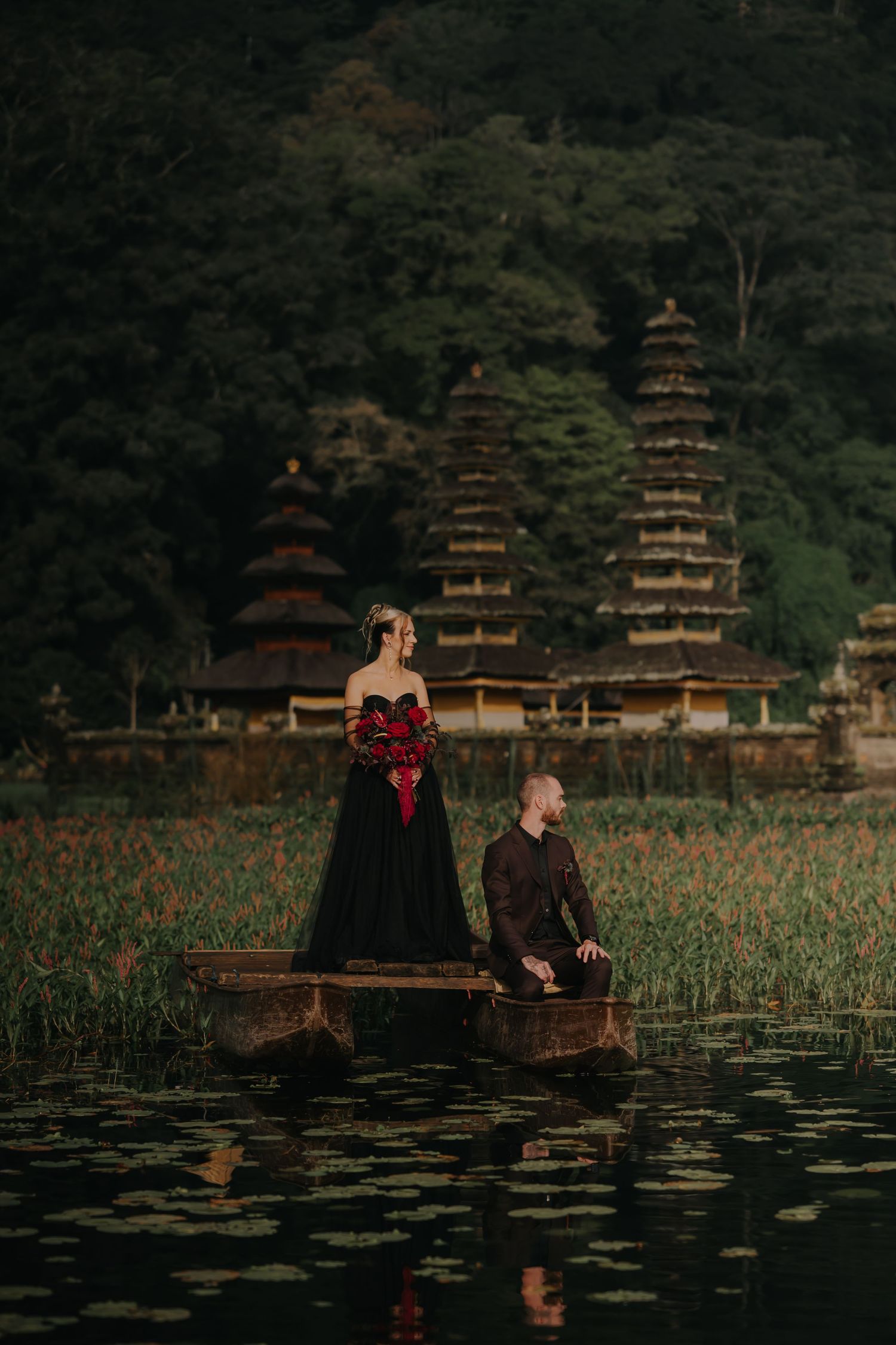 A dramatic photo shoot in a lake with pagodas visible in the background and lily pads in the foreground.