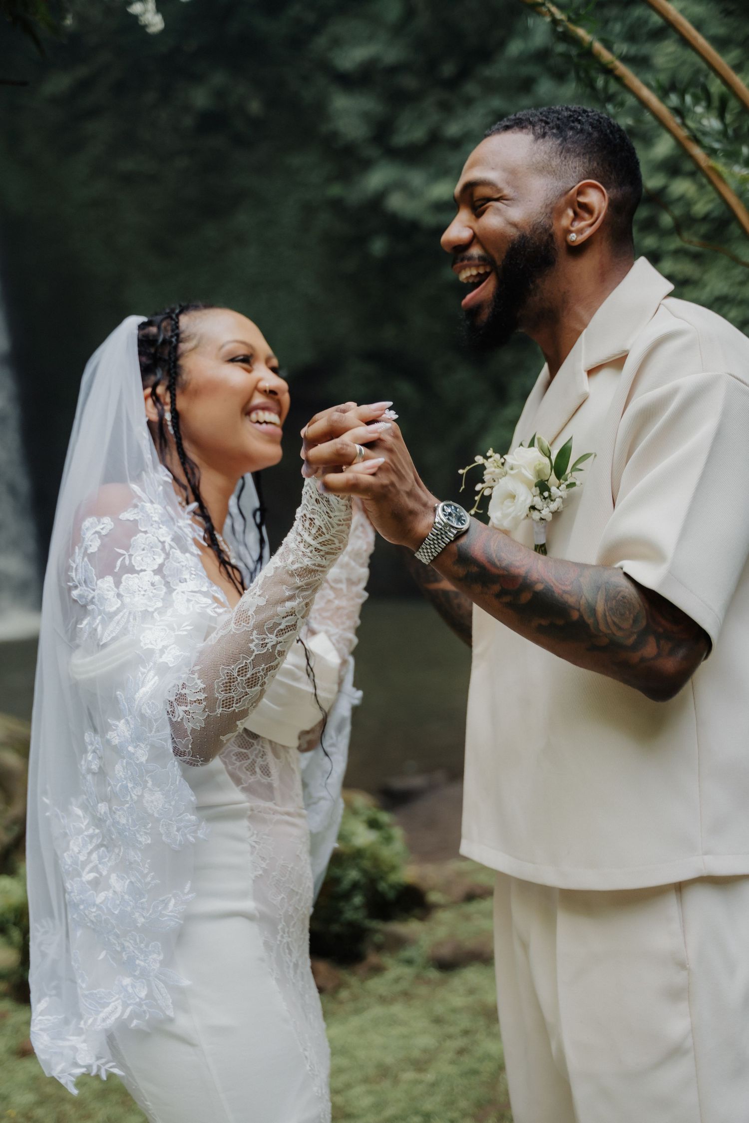 Joyful bride and groom hold hands and laugh together in a lush tropical wedding setting.