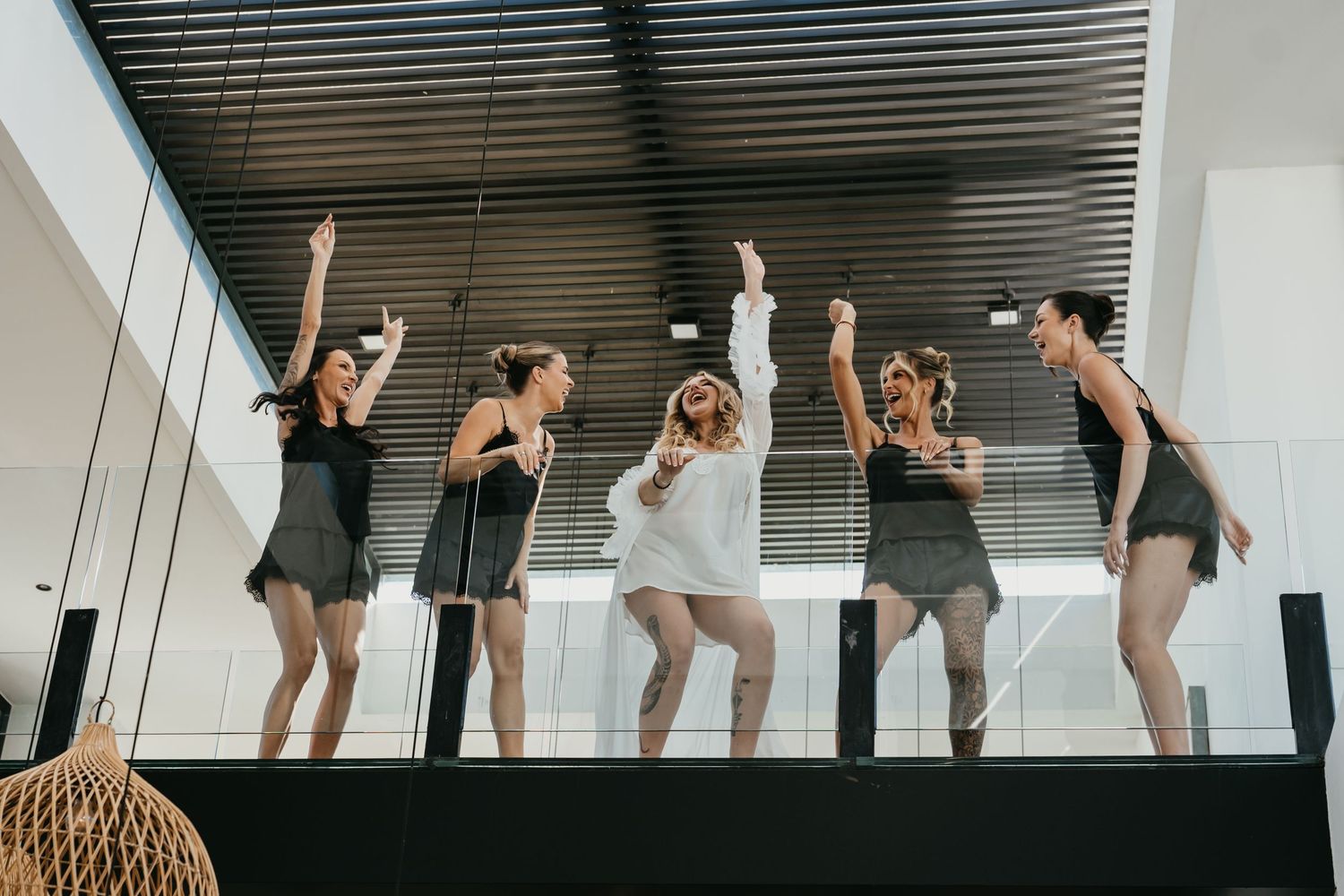 Group of five women celebrating and dancing together indoors with arms raised in a modern venue.