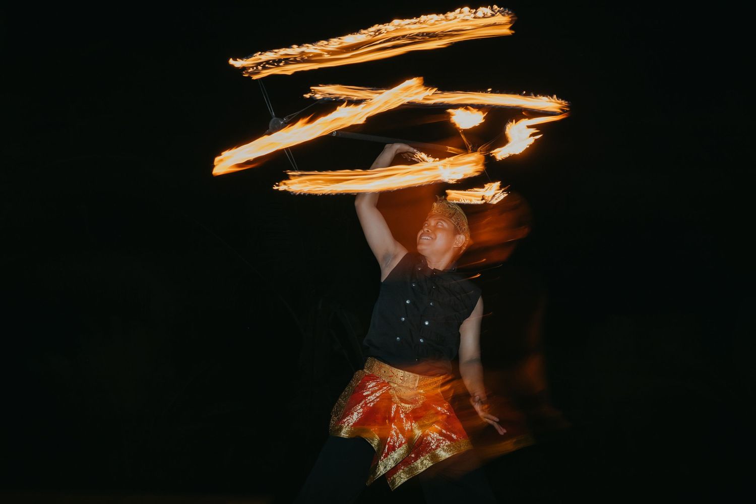 Fire dancer performing a dramatic long-exposure spinning routine against a dark background at a wedding.