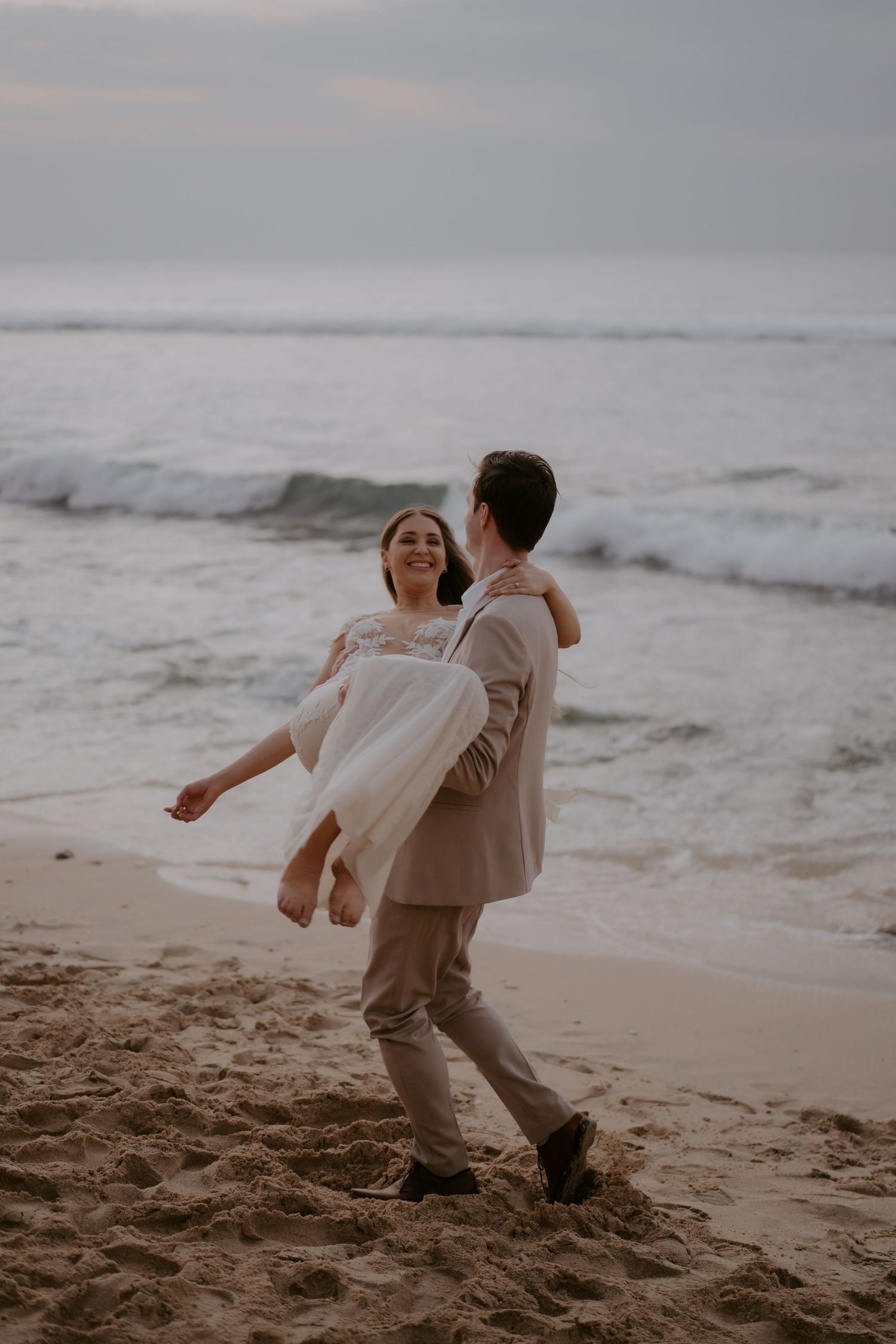 A couple dances playfully together on a misty beach at sunset, creating a romantic and carefree moment by the ocean.