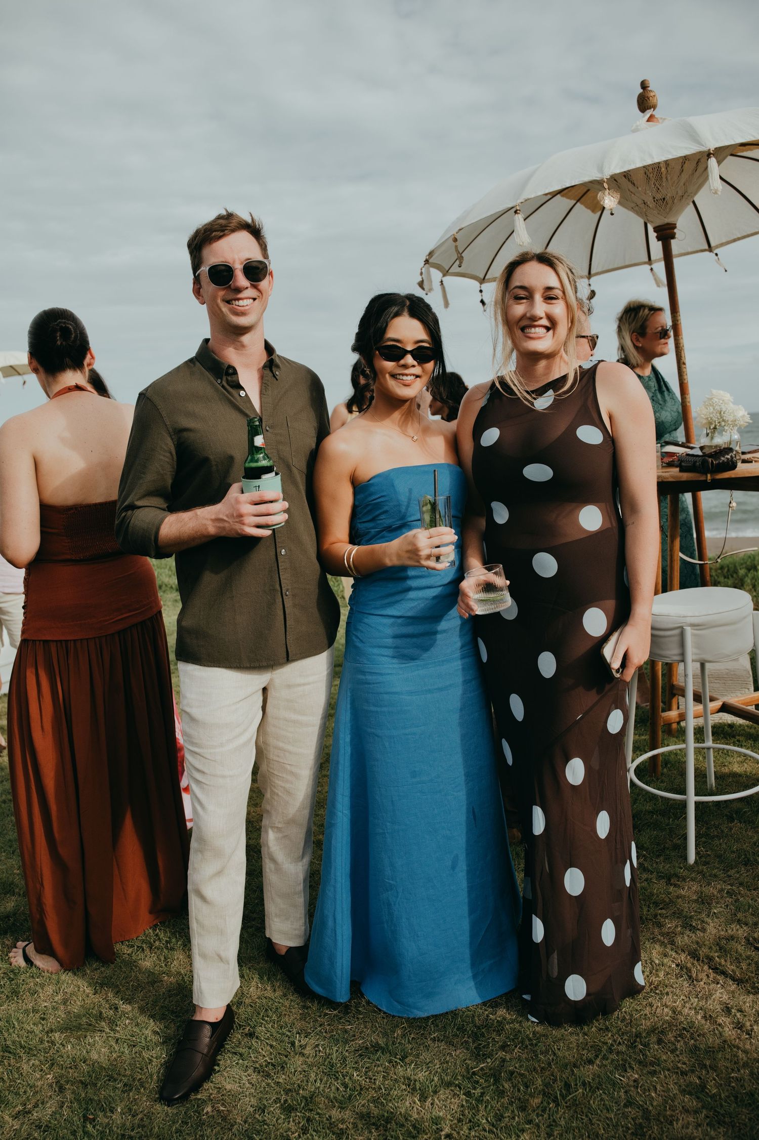 Wedding guests posing outdoors, wearing a polka dot dress and blue strapless gown.