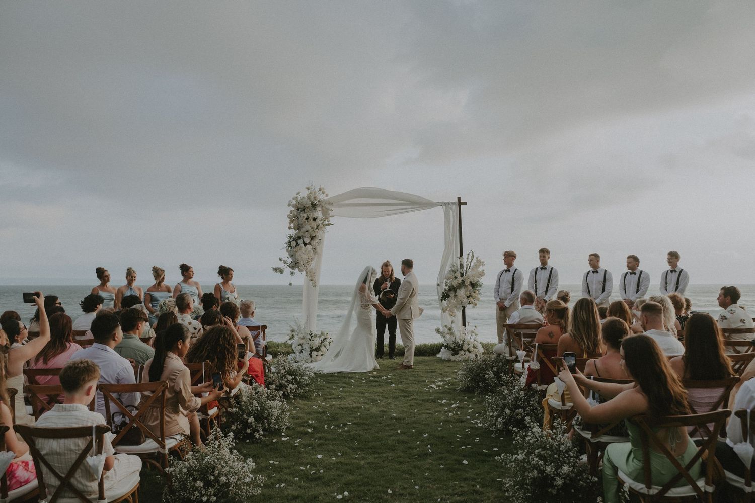 Wedding guests gather on a hilltop overlooking a scenic landscape during an outdoor ceremony.