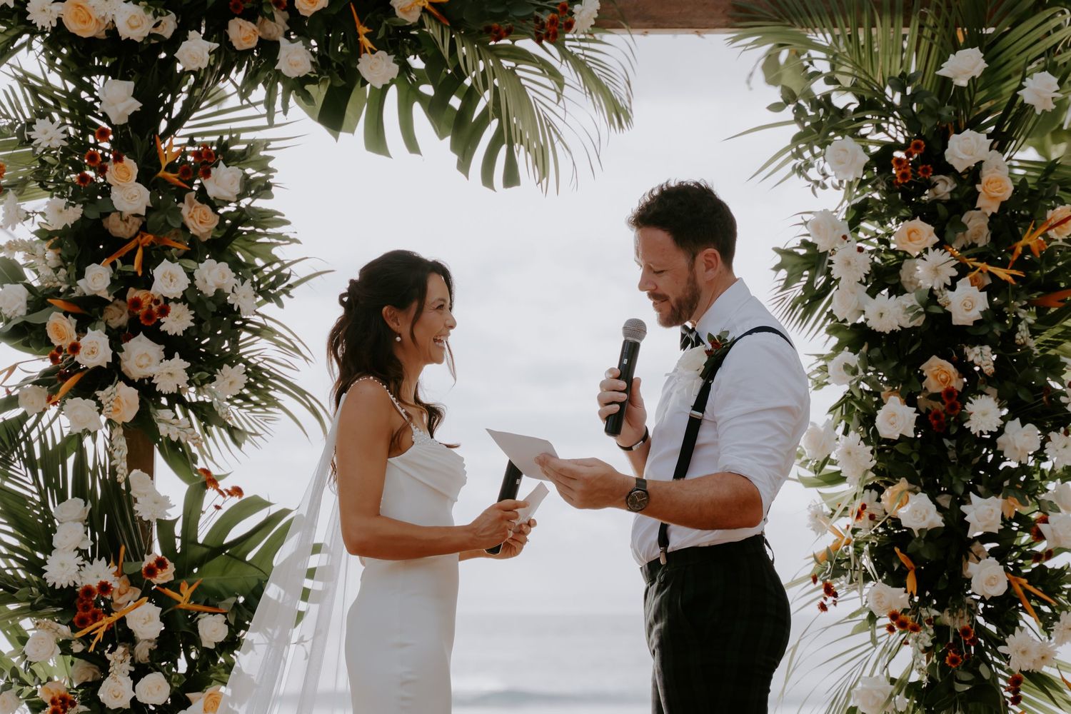 A romantic beach wedding ceremony with tropical floral arrangements and ocean backdrop.