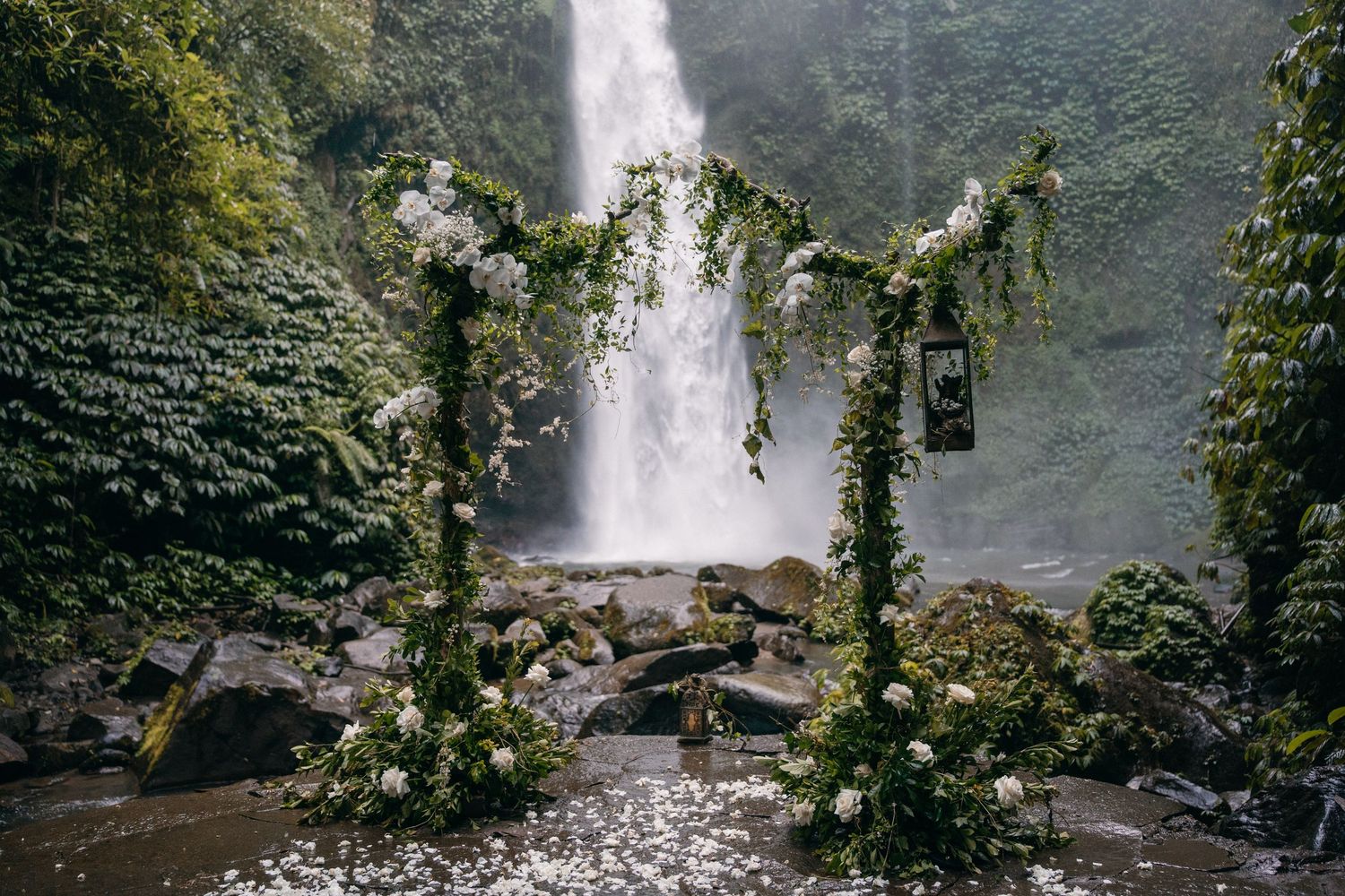 A majestic waterfall cascades down a rocky cliff face surrounded by lush tropical vegetation in a rainforest setting.
