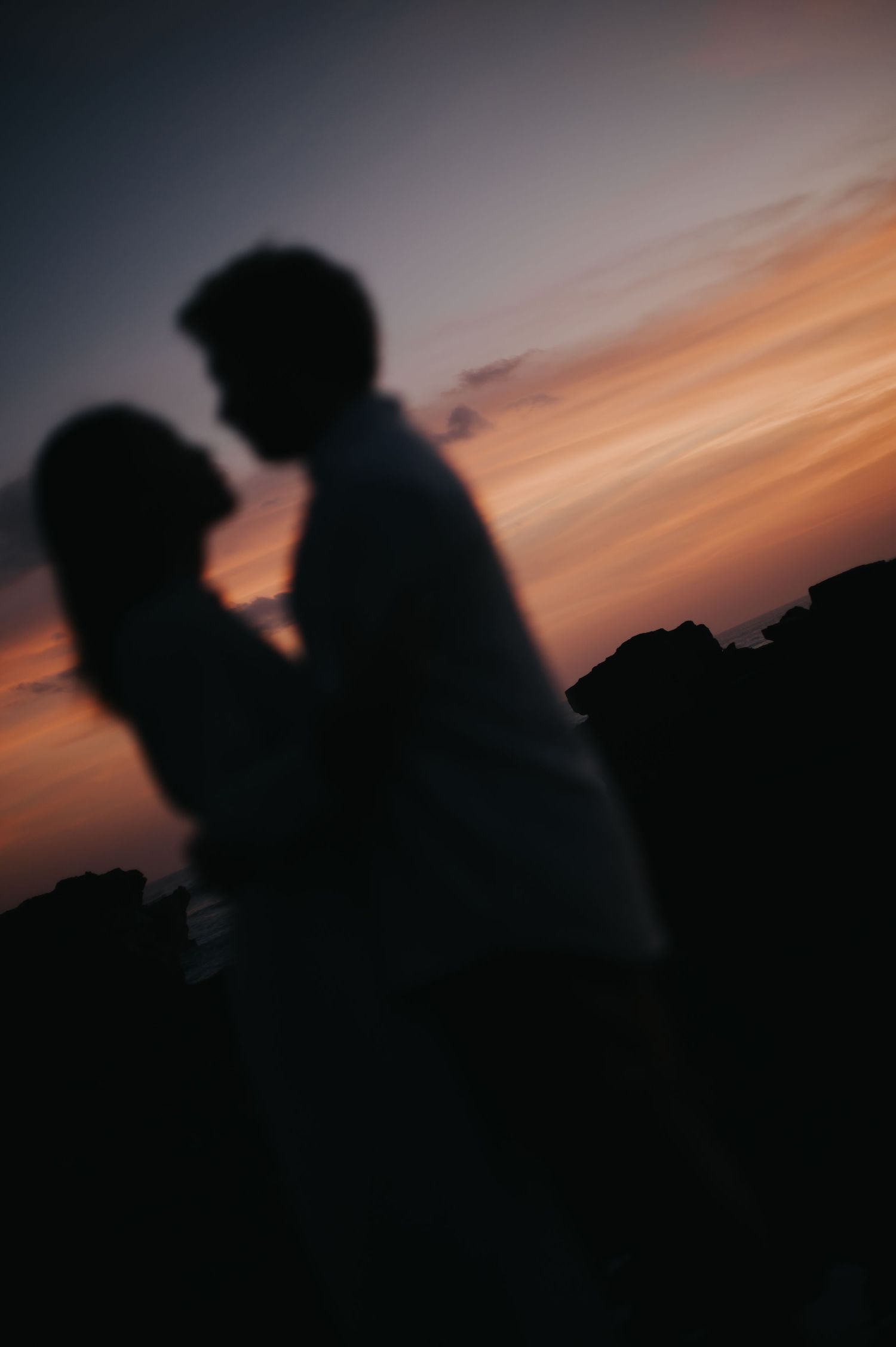 Silhouettes of two people in profile against a vibrant orange and pink sunset sky.