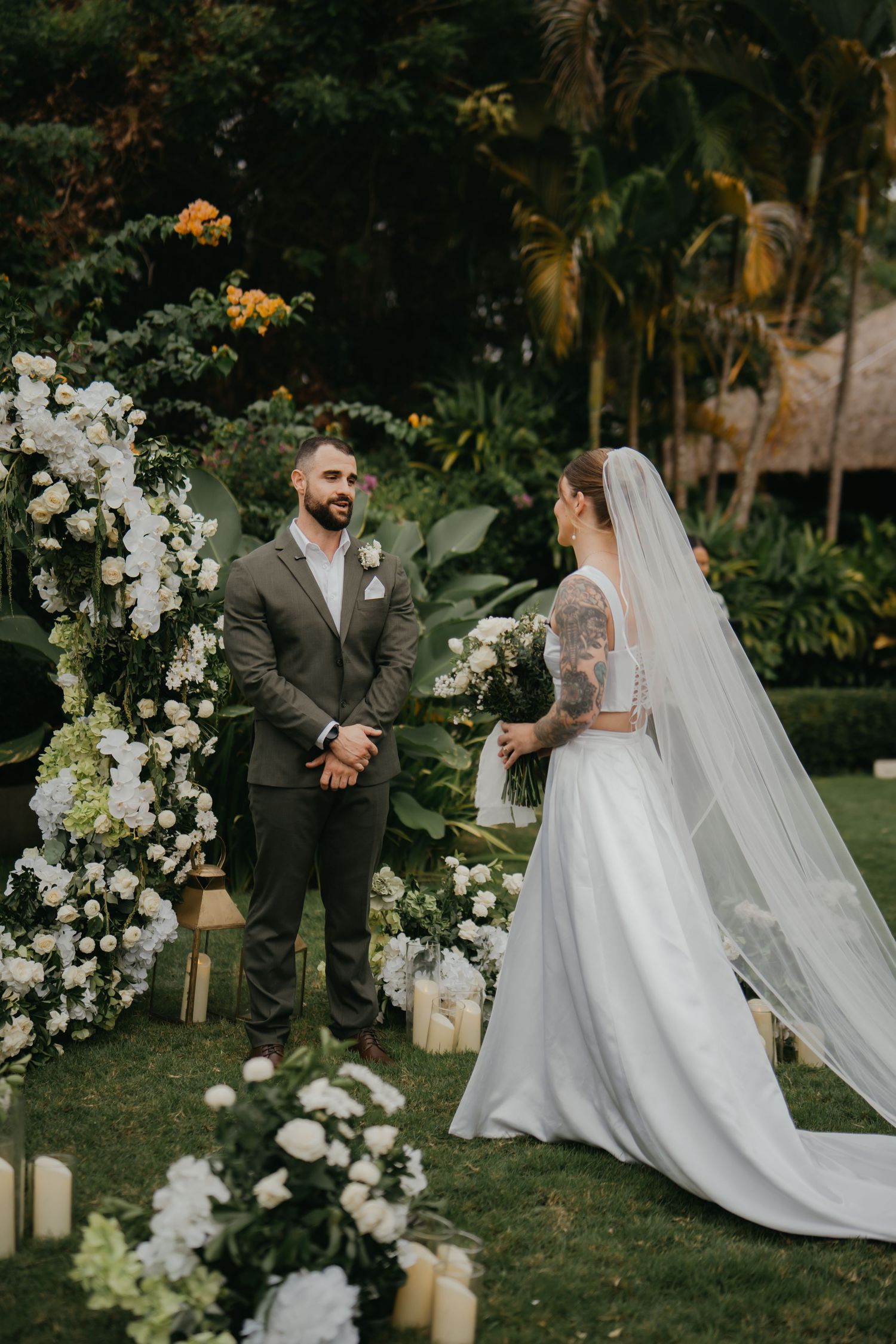 Bride and groom exchange vows at outdoor garden wedding ceremony with white floral arch.