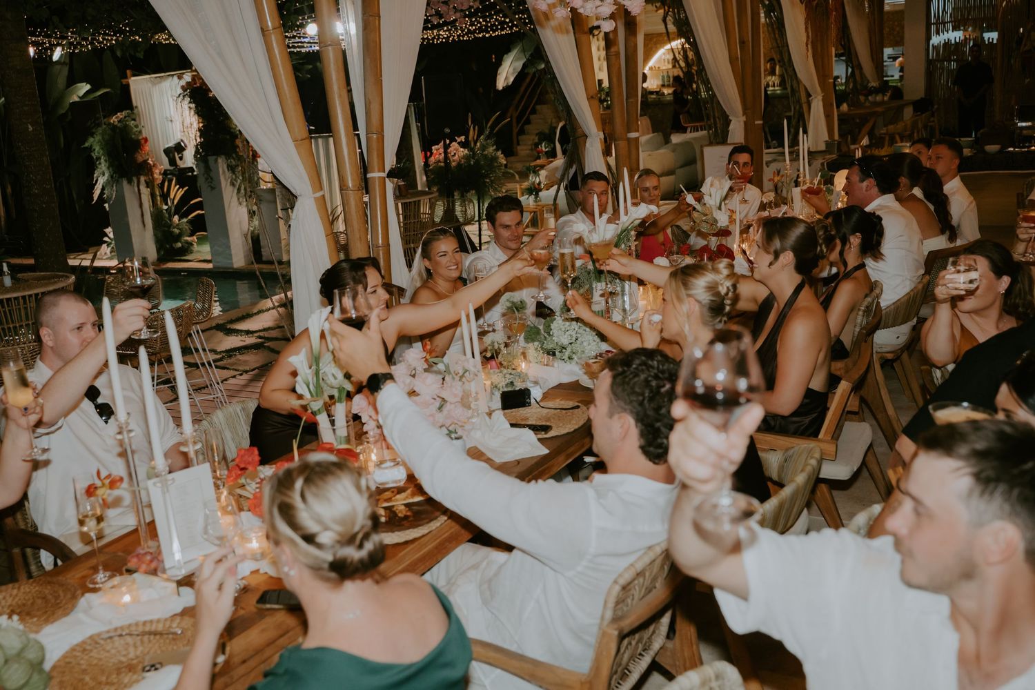 Wedding guests raising glasses in a toast at an elegantly decorated outdoor reception dinner.