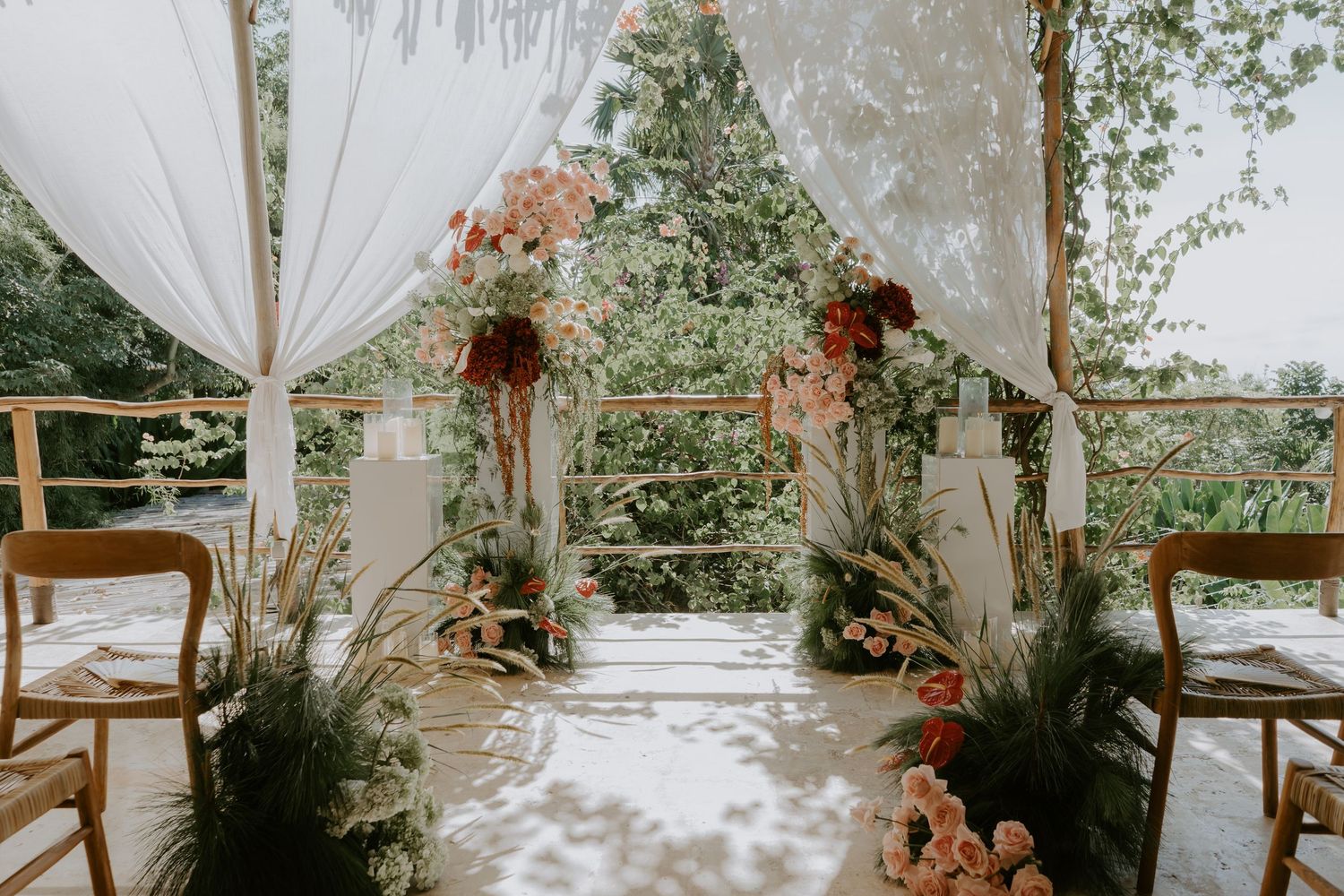 Romantic outdoor wedding ceremony arch with white draping, blush pink florals, and lush garden backdrop.