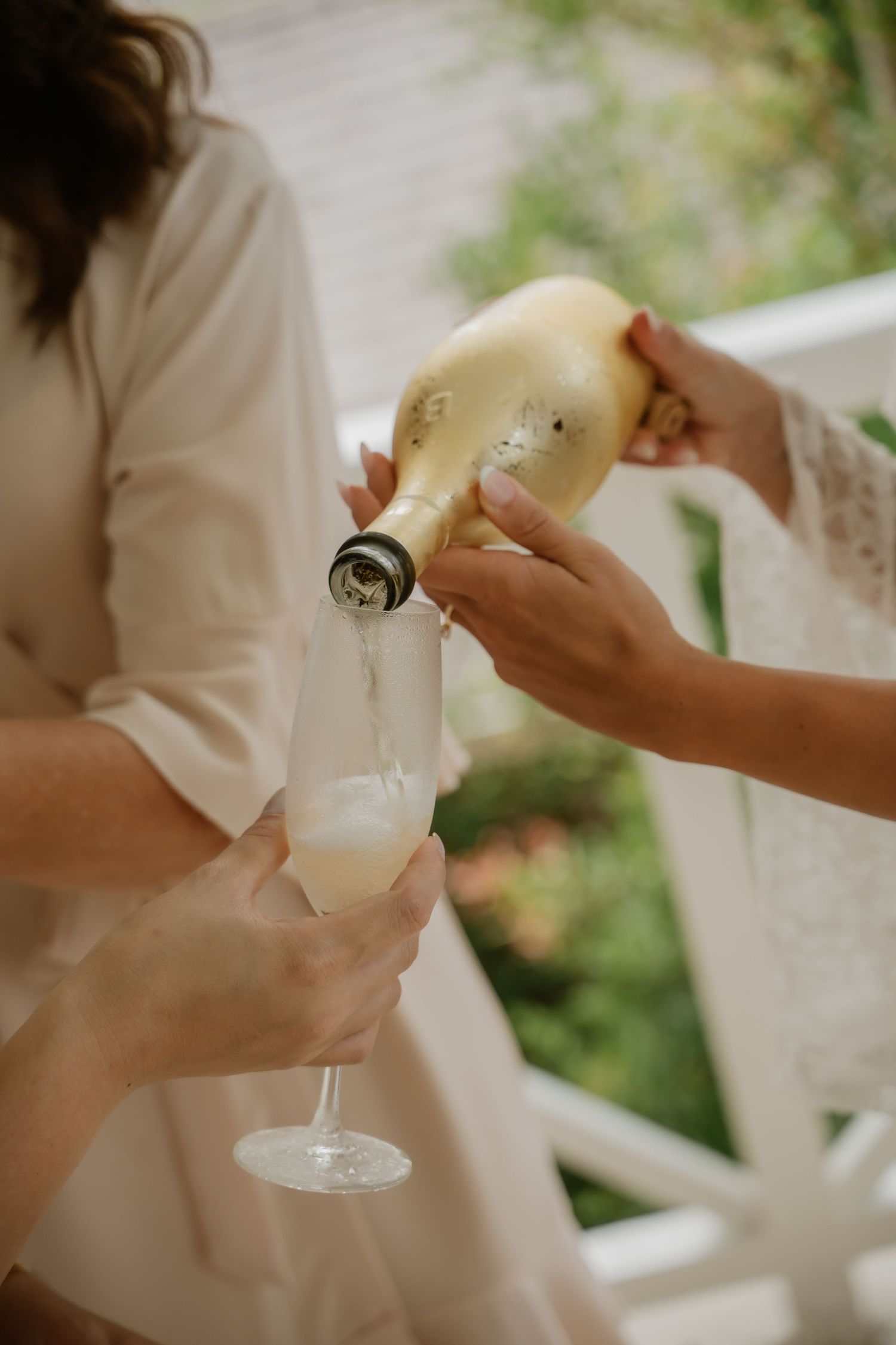 Close-up of champagne being poured into a flute at a bridal getting-ready celebration outdoors.