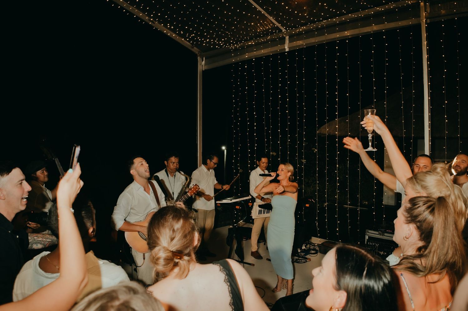 Live band performing as wedding guests dance and celebrate under starlit canopy at outdoor reception.