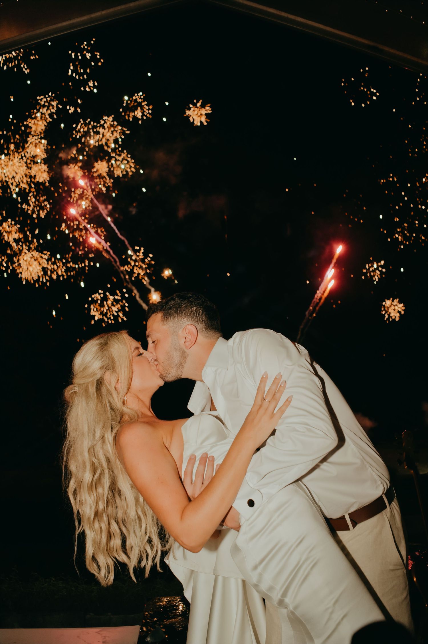 Bride and groom share a romantic kiss surrounded by dazzling fireworks and sparklers at their wedding reception.