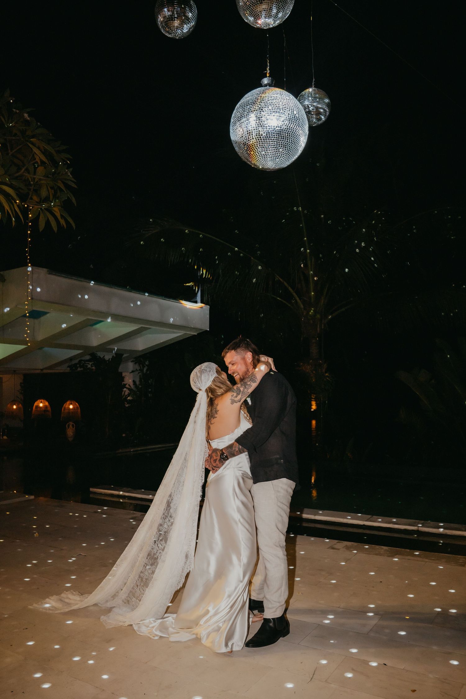 Bride and groom share first dance under glowing disco balls at an outdoor nighttime wedding reception.