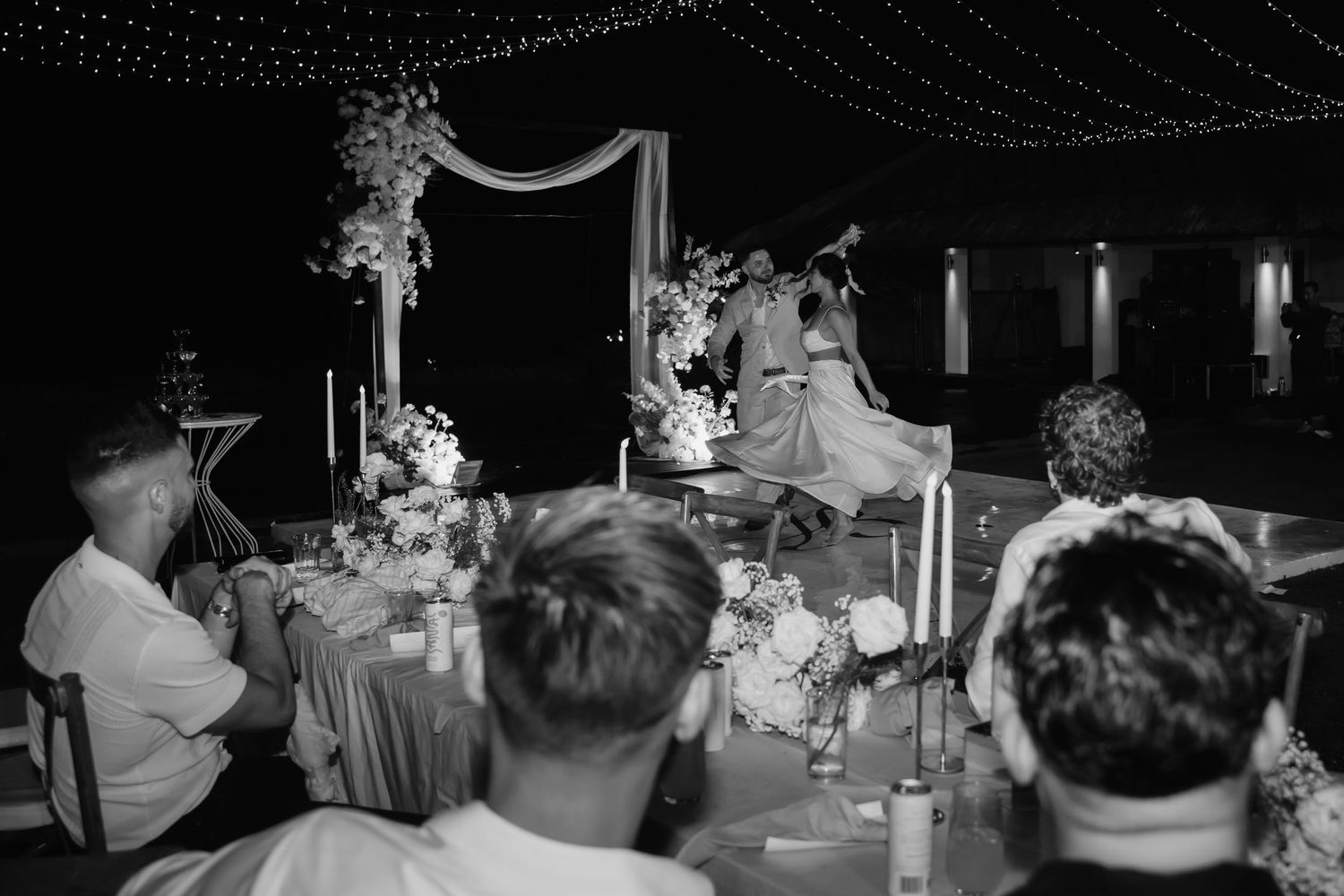 Black and white photo of a wedding reception dance floor with guests enjoying themselves in a dimly lit venue.