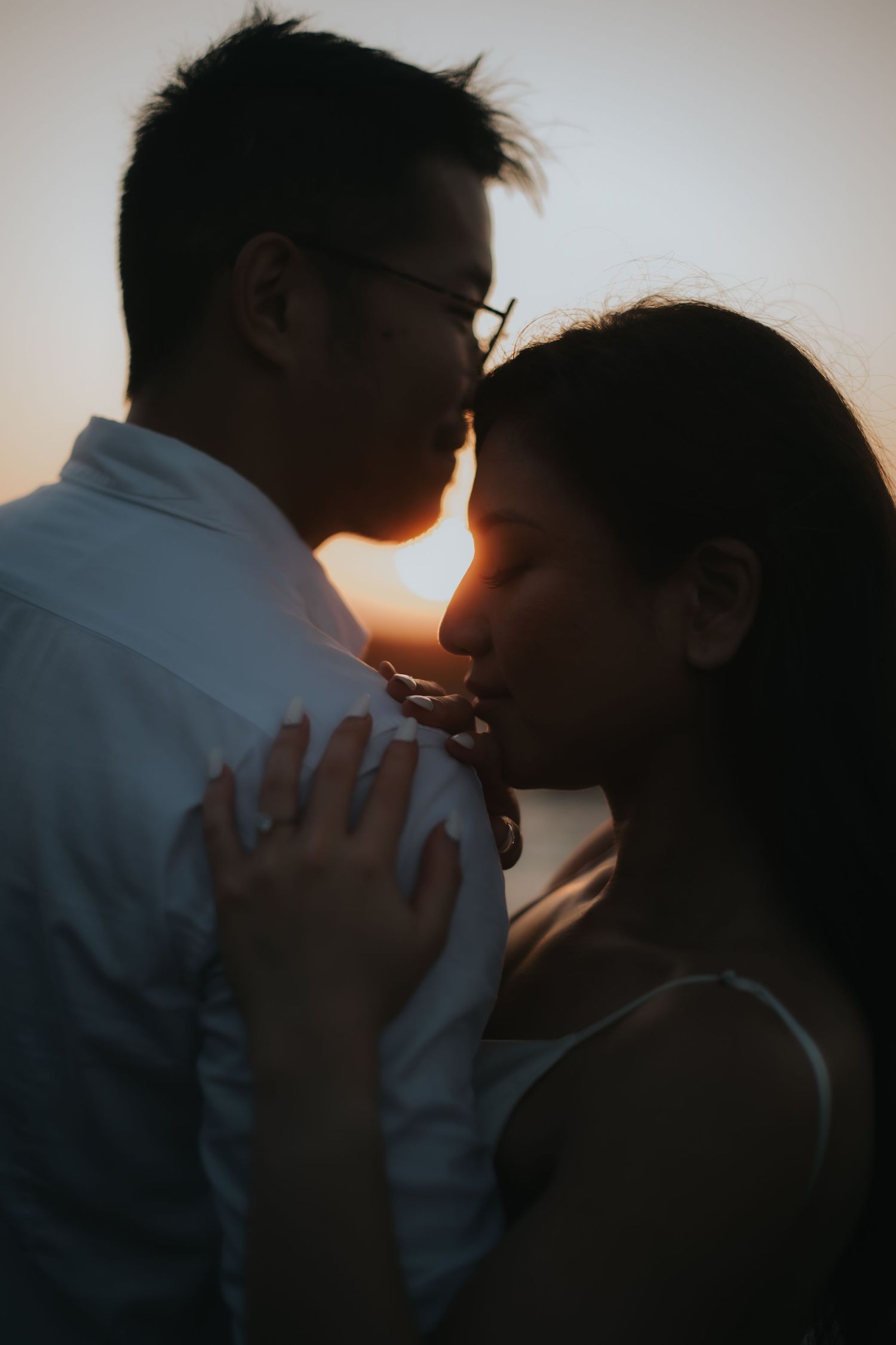 A couple shares a romantic moment at sunset, silhouetted against a warm golden sky in an intimate embrace.