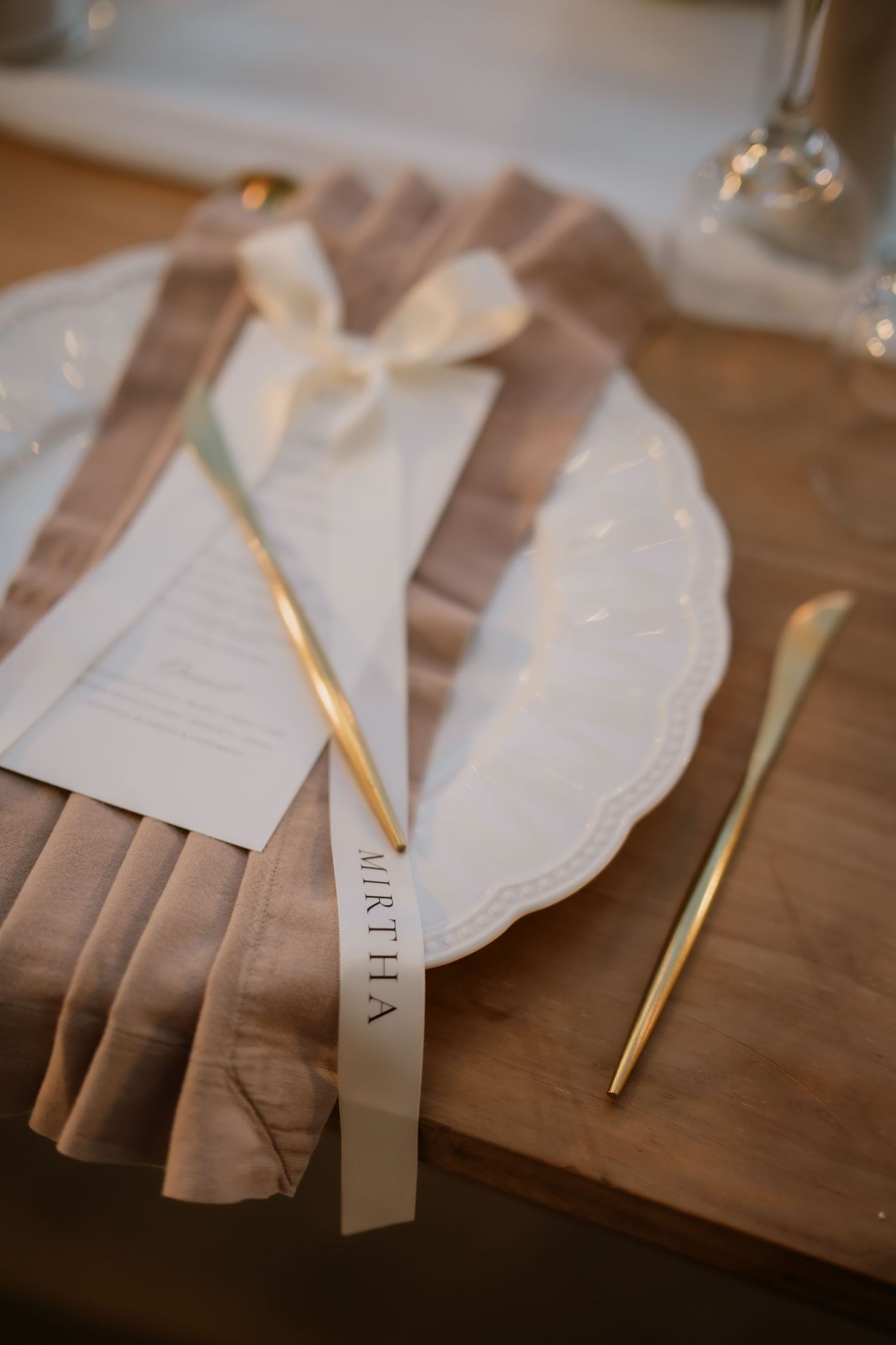 Elegant wedding place setting with gold cutlery, ruffled napkin, and personalized name card on white plate.