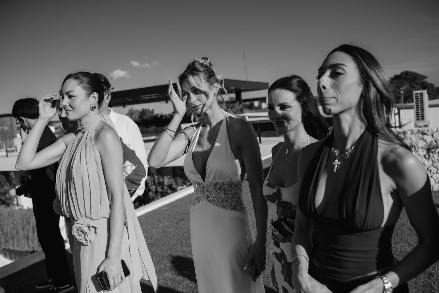 Black and white photo of stylish female wedding guests socializing outdoors at tropical venue.