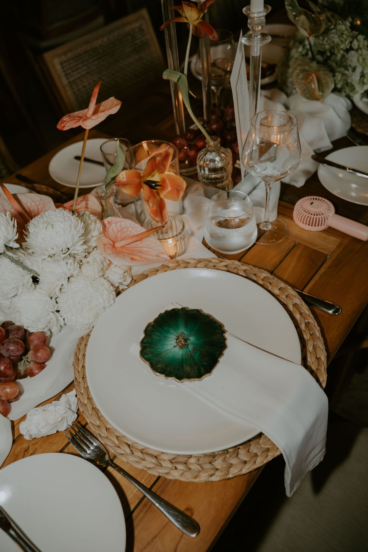 Tropical wedding tablescape with green agate charger plate, white florals, anthurium blooms, and candlelight.