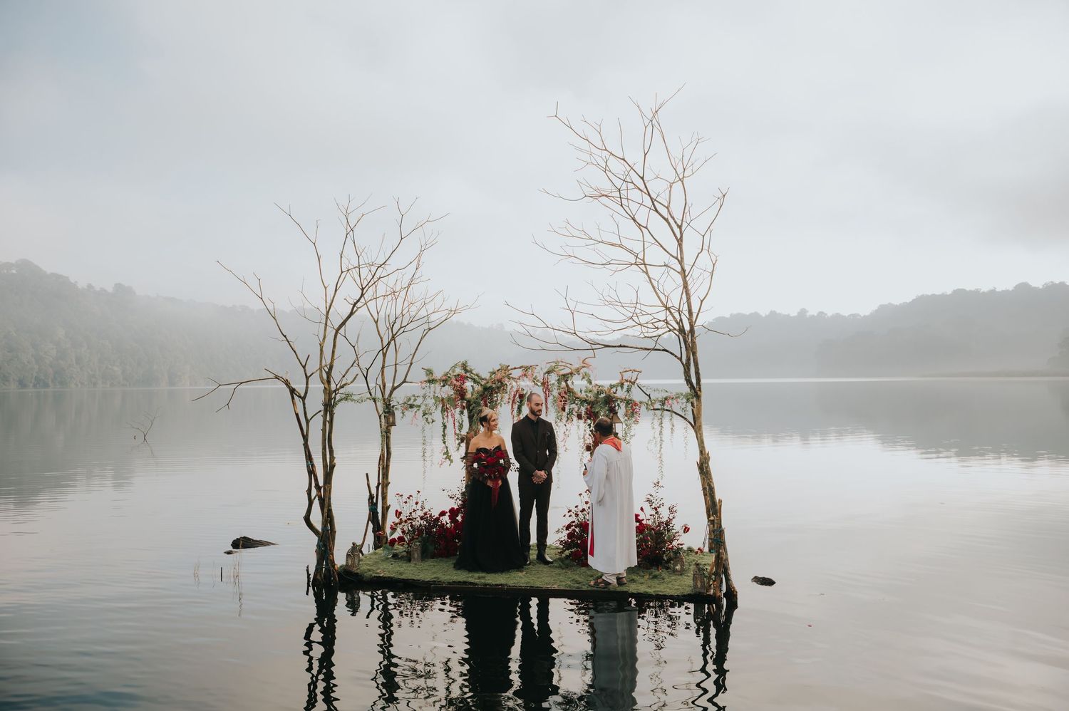 Ethereal lakeside wedding ceremony setup with bare trees emerging from misty waters.