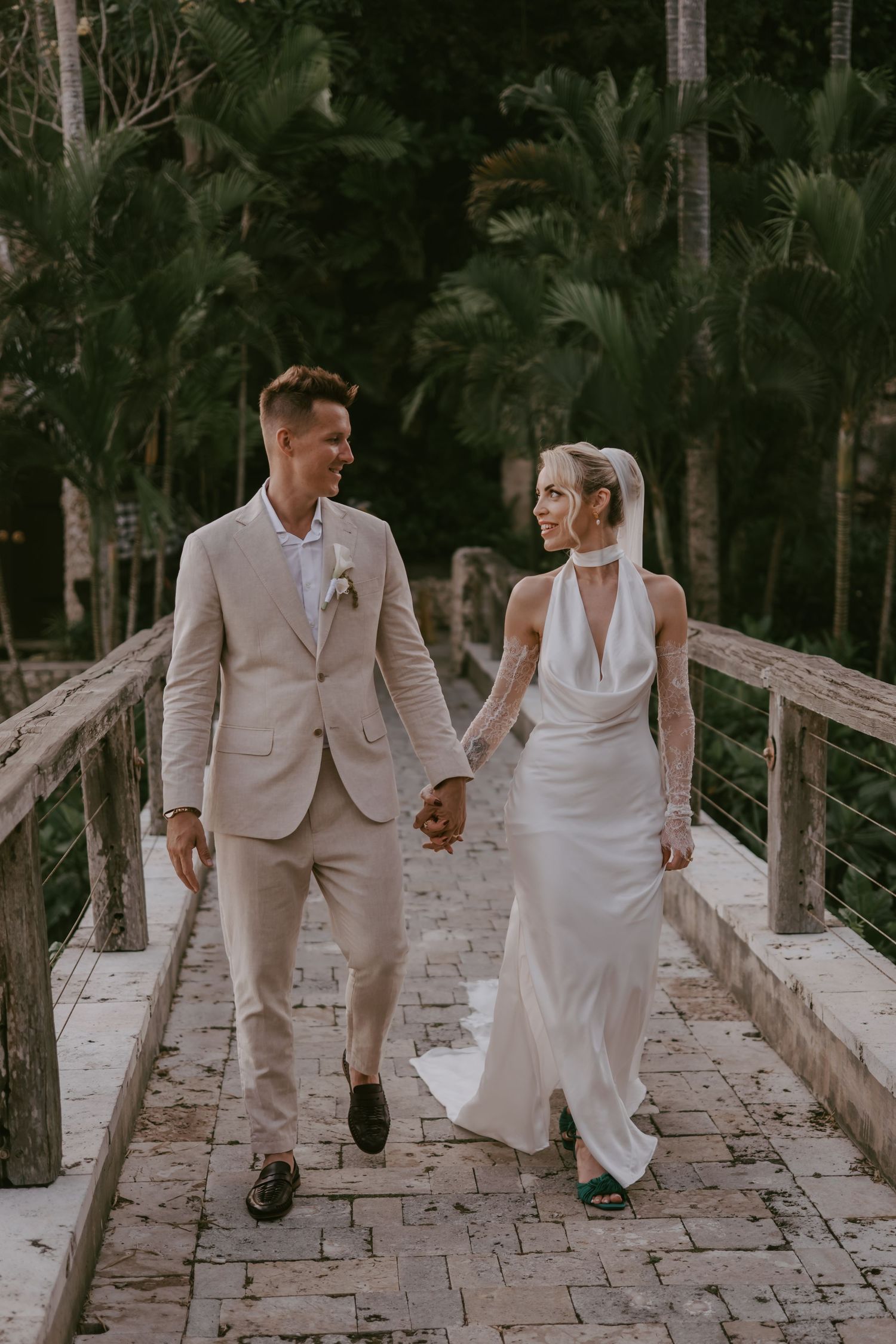 Wedding couple walking hand in hand on a stone pathway surrounded by trees.