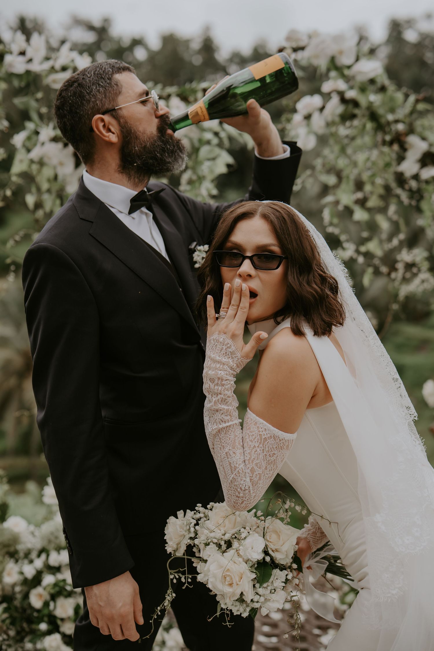 A romantic wedding photo series showing a couple drinking wine together in a garden setting with white flowers.