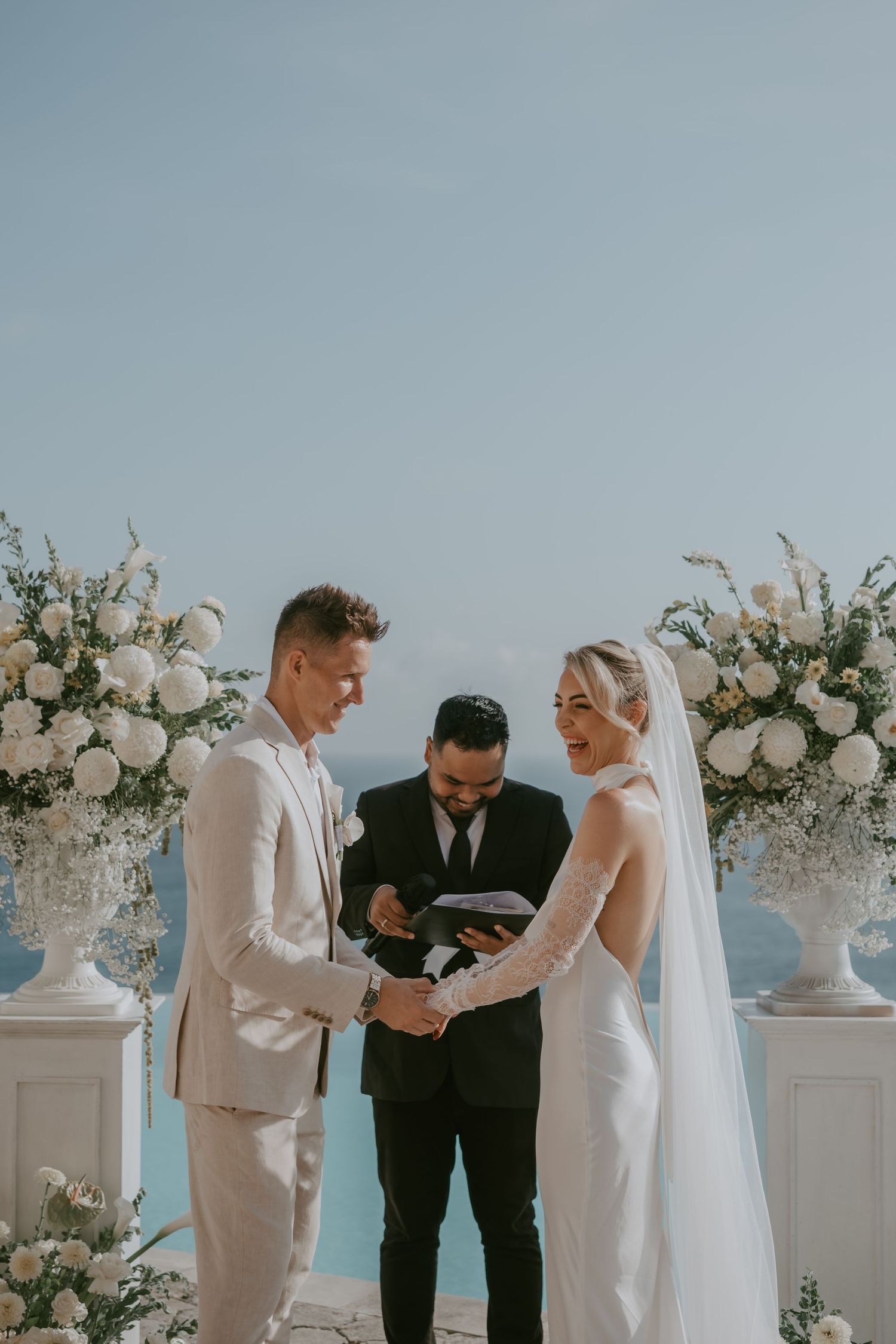 Elegant wedding ceremony by the ocean with white floral arrangements and columns.