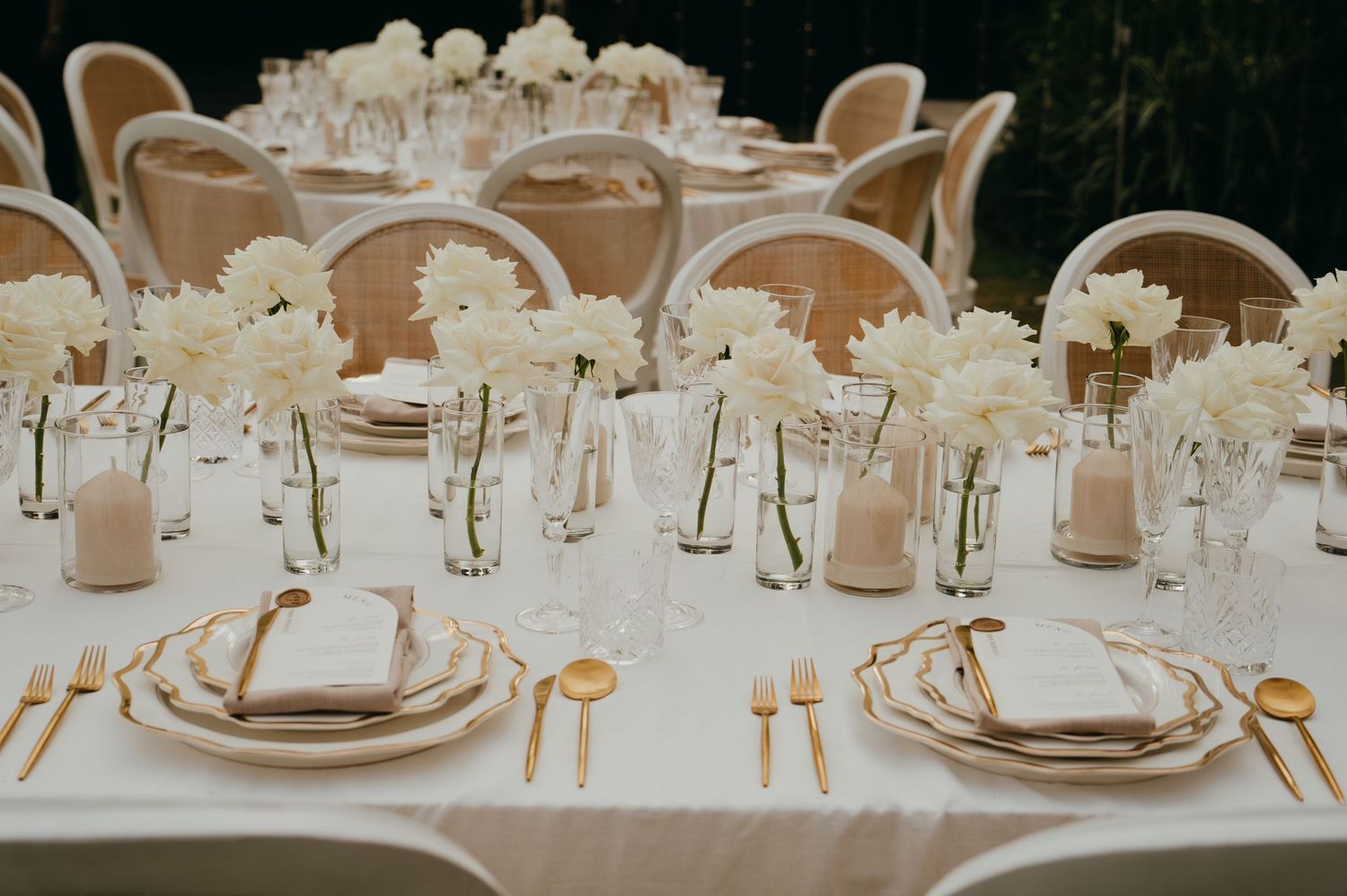 Elegant wedding reception table set with white dahlias, gold cutlery, and white linen napkins.