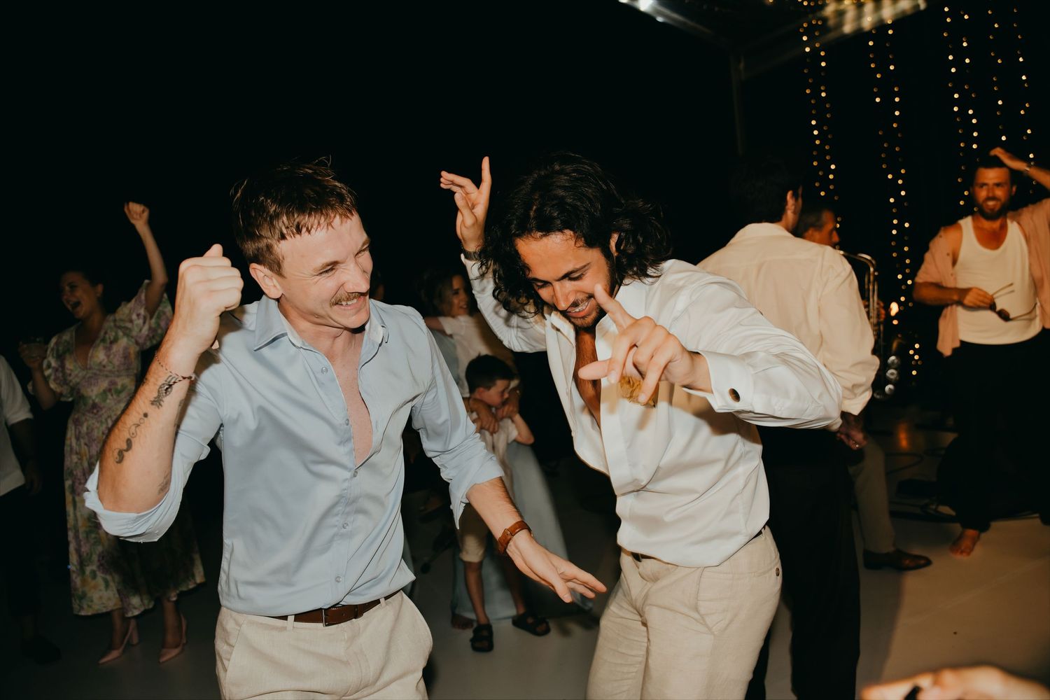 Two male wedding guests dance energetically on the dance floor at a lively wedding reception.