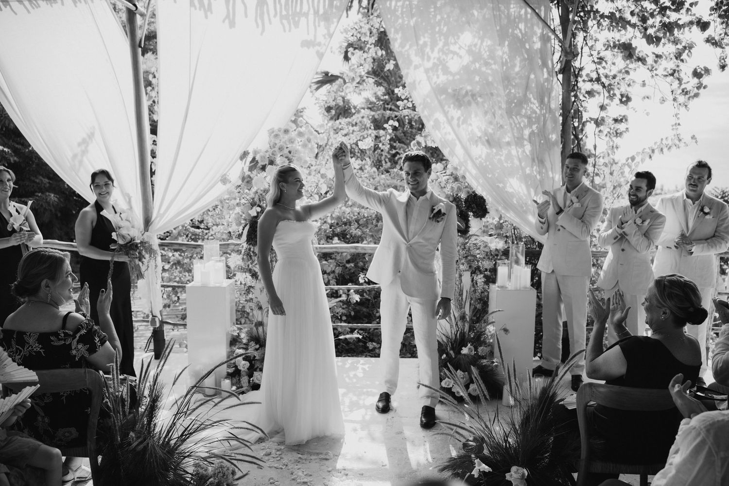 Black and white photo of bride and groom celebrating at the altar surrounded by wedding guests.