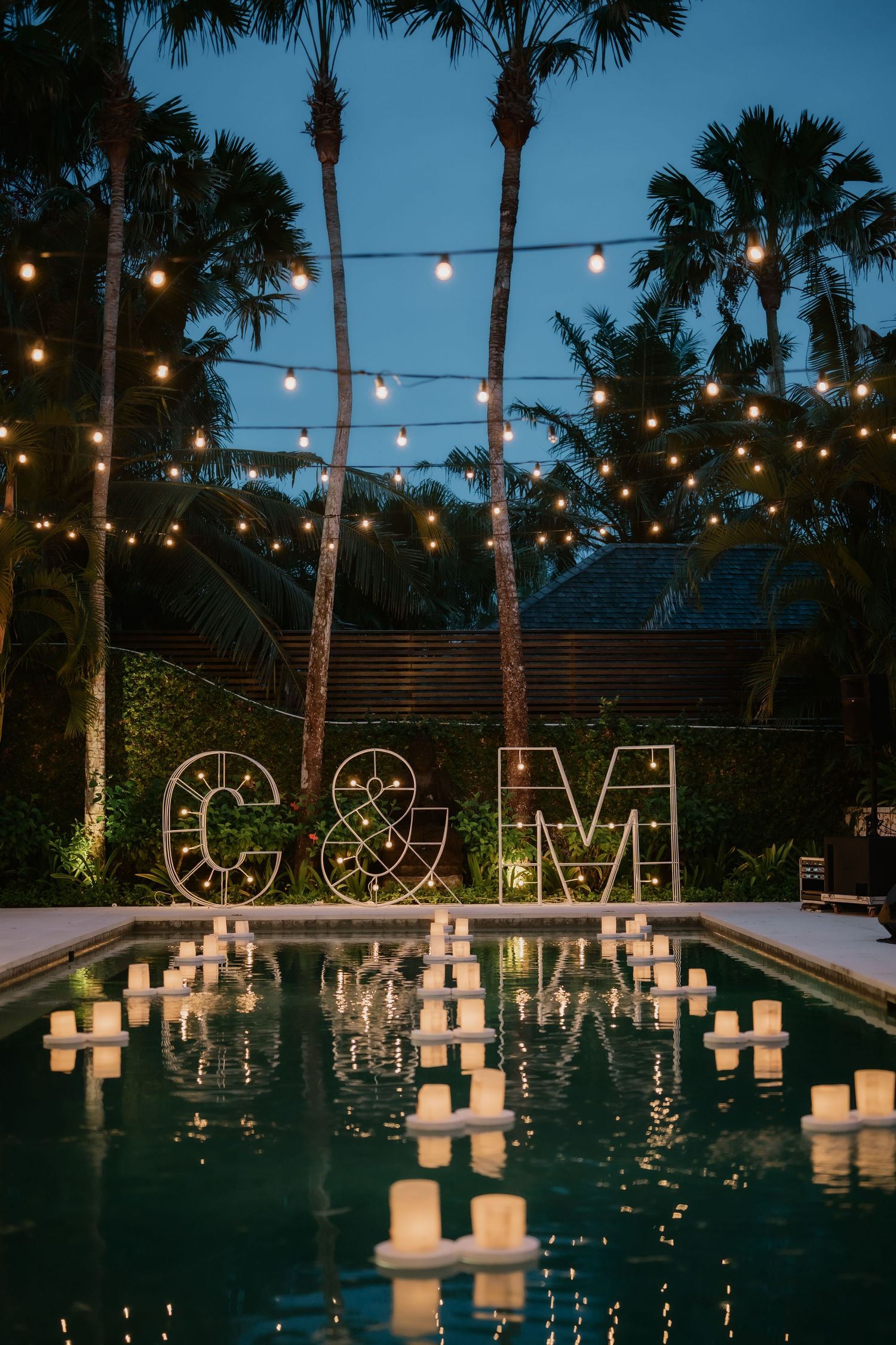 Wedding monogram letters C&M beside pool with floating candles and string lights at night reception.