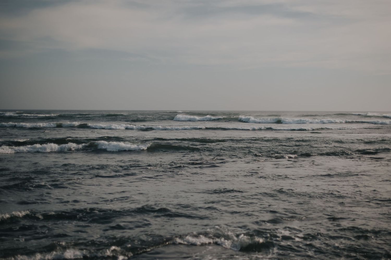 Dramatic panoramic view of stormy ocean waves rolling under a moody gray sky at dusk.