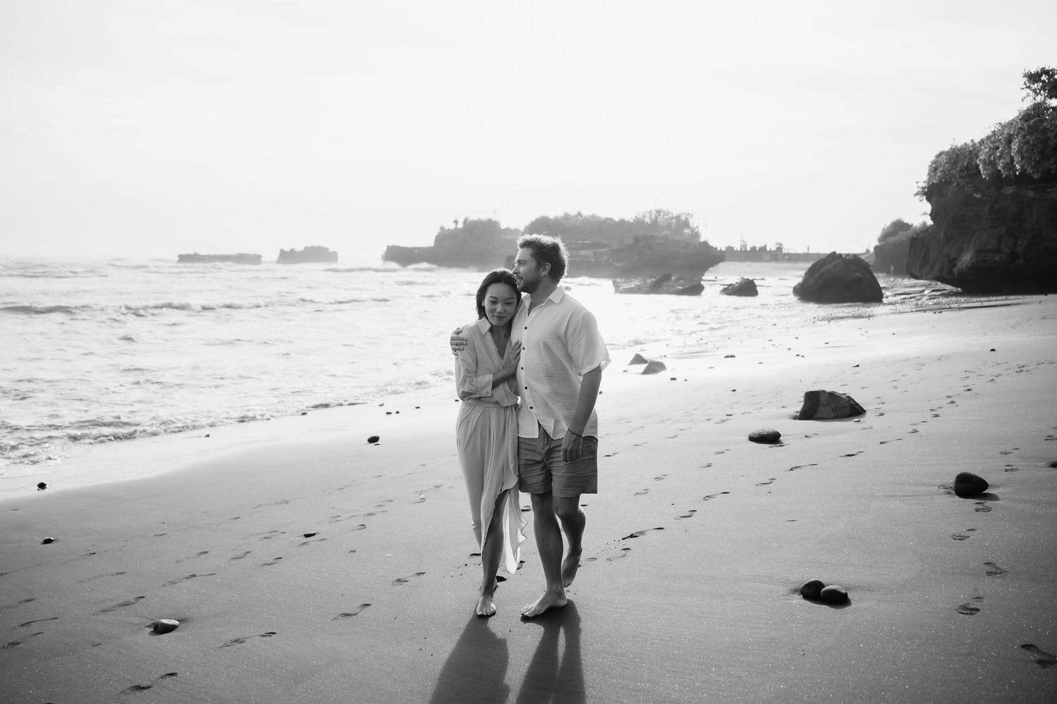 A romantic couple embraces on a misty beach during sunset creating a dreamy silhouette against the ocean waves.