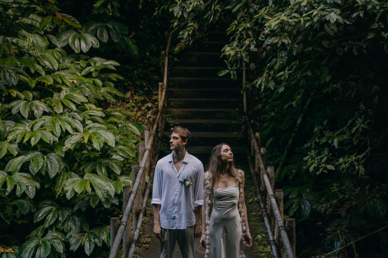 Couple walks together through lush garden pathway surrounded by green foliage and natural light.