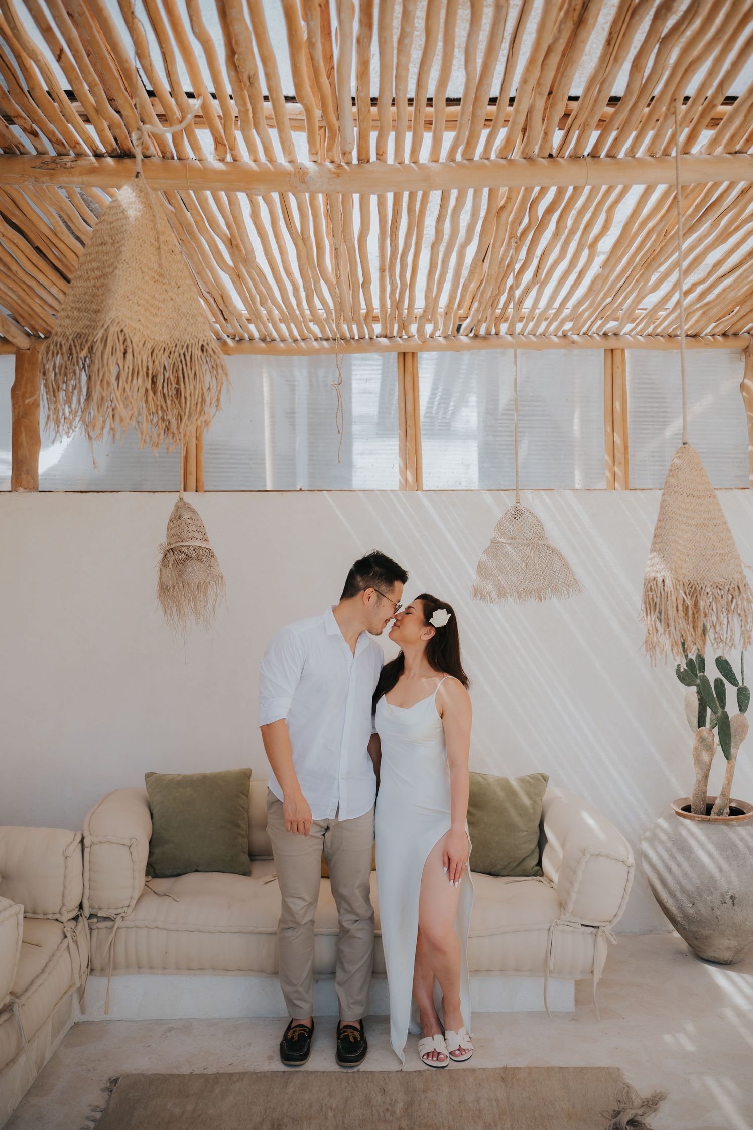 Couple sharing a romantic kiss in a boho-styled venue with bamboo ceiling and macrame decor.