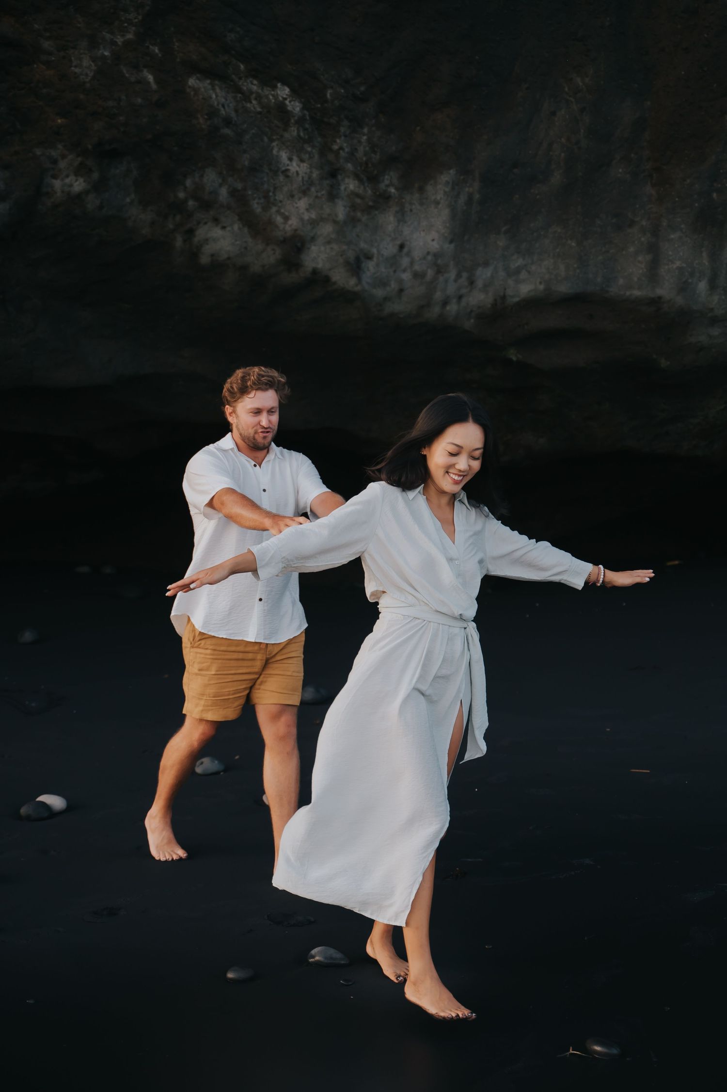 Two dancers in white and tan outfits perform a graceful leaping dance sequence against a dark background.