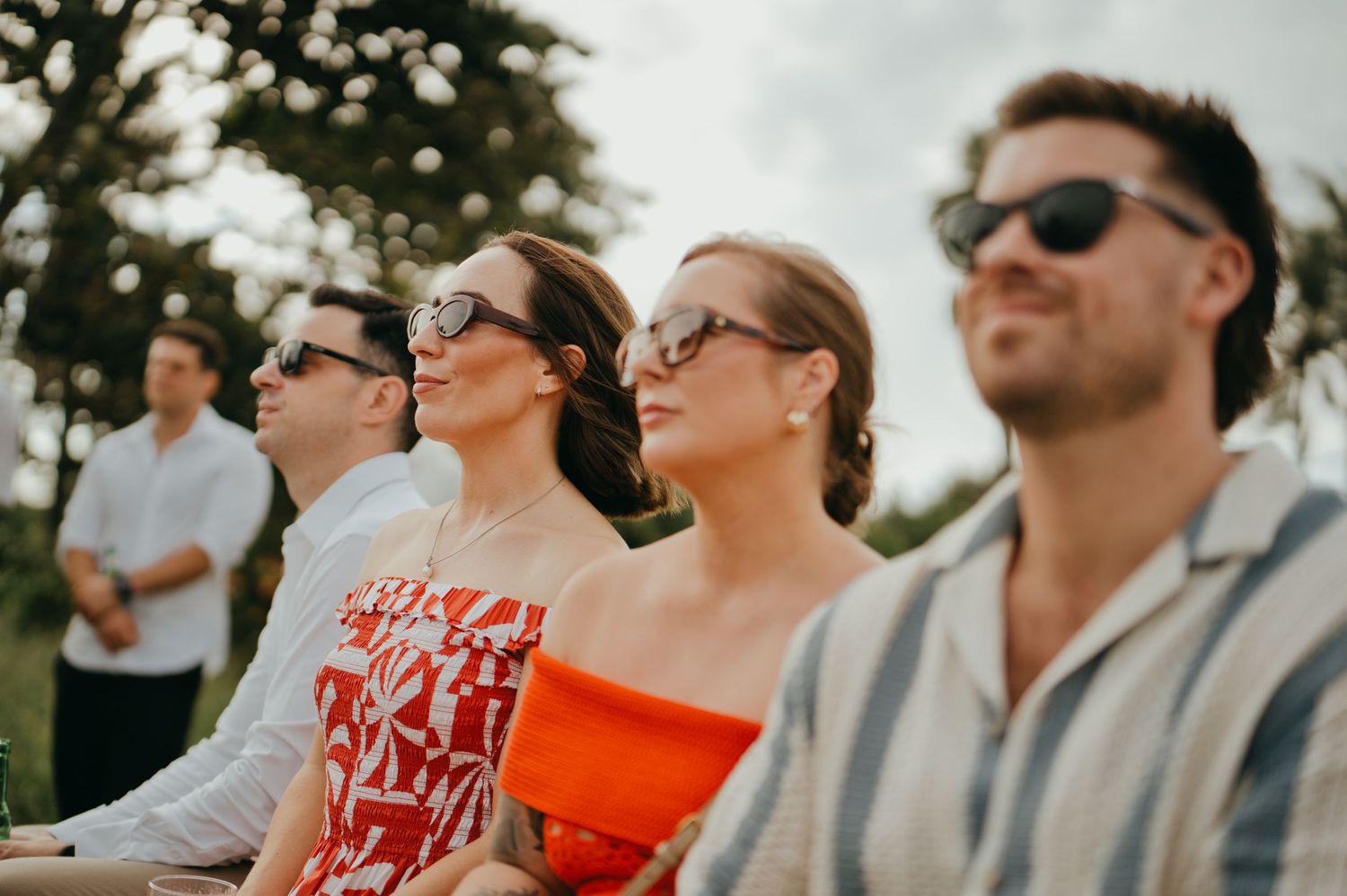 Wedding guests in sunglasses enjoying outdoor ceremony under natural light.