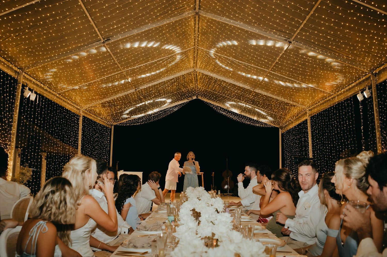 Bride and groom share a toast under a stunning fairy light canopy at their wedding reception dinner.