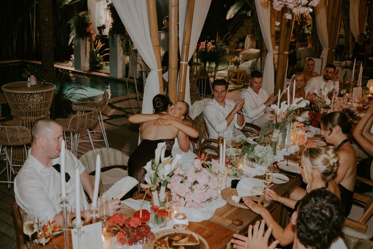 Bride and groom sharing emotional embrace at wedding reception table surrounded by floral centerpieces.