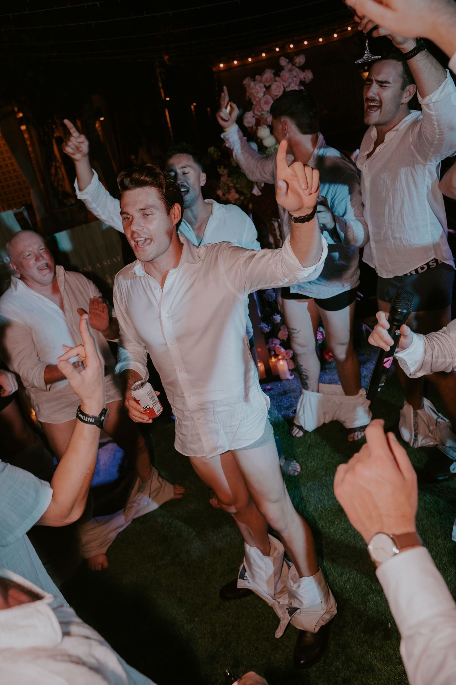Guest in white shirt dancing enthusiastically at lively outdoor wedding reception under string lights at night.