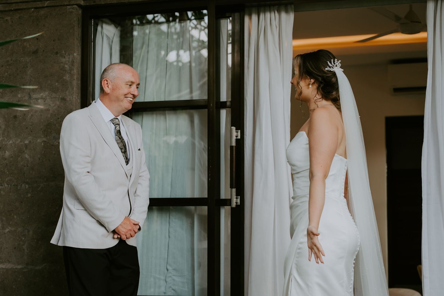 Father seeing bride in white wedding dress and veil for the first time, emotional first look moment.