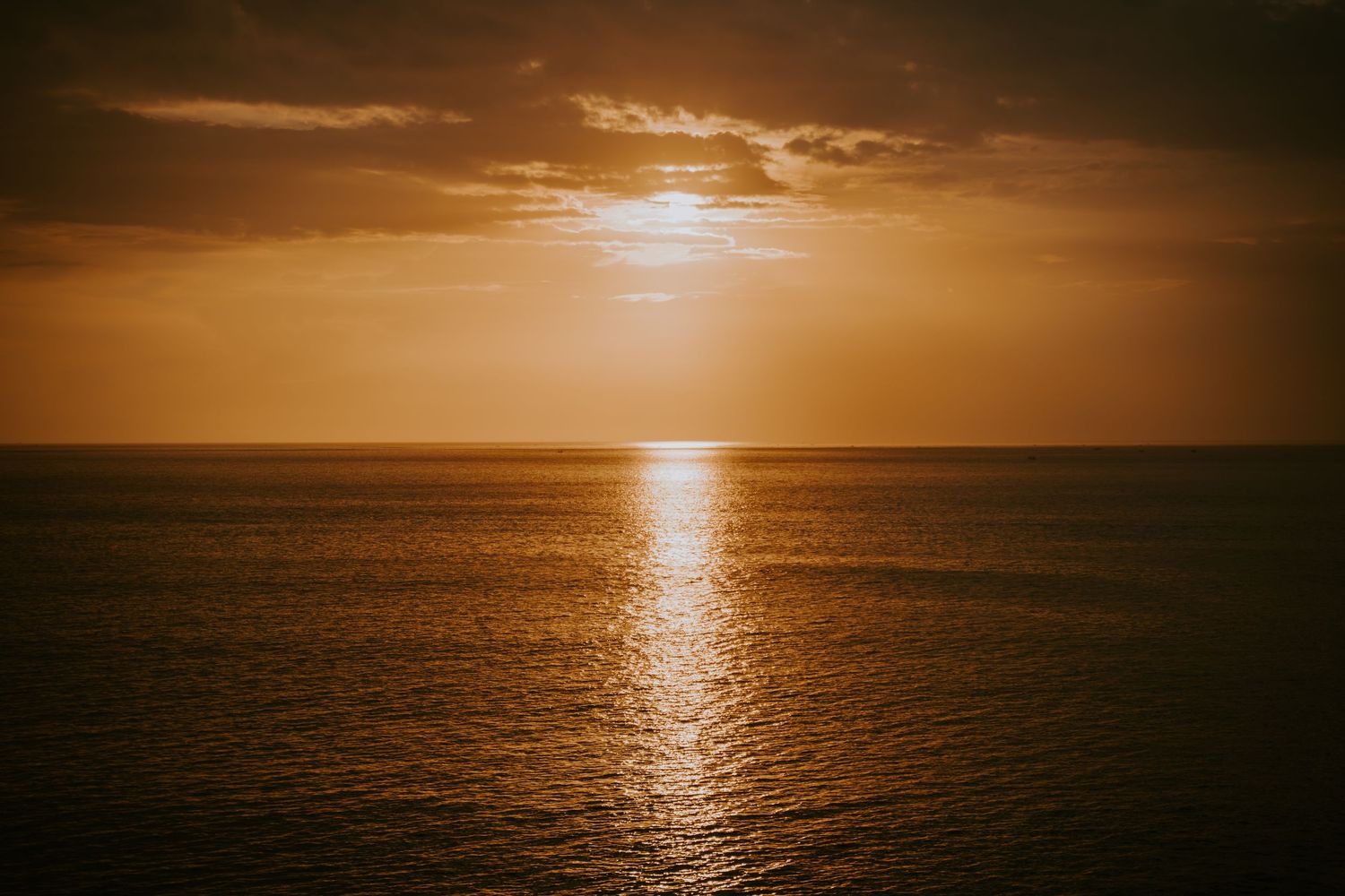 Golden sunset over a calm ocean horizon with warm orange and amber tones reflecting on the water surface.