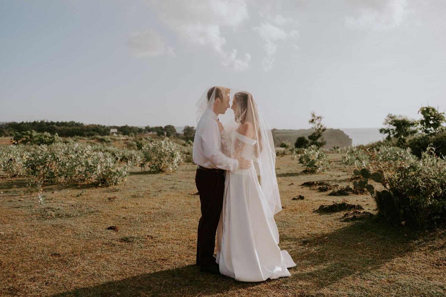 Bride and groom share a romantic kiss in an open field during their outdoor destination wedding ceremony.
