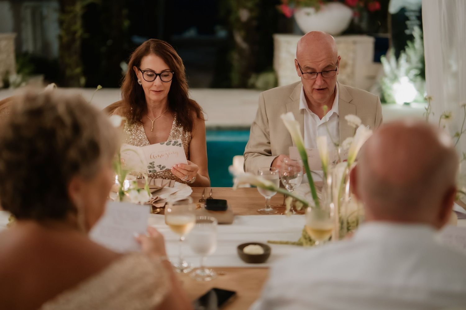 Older couple reads from papers at candlelit wedding reception dinner table during toasts.