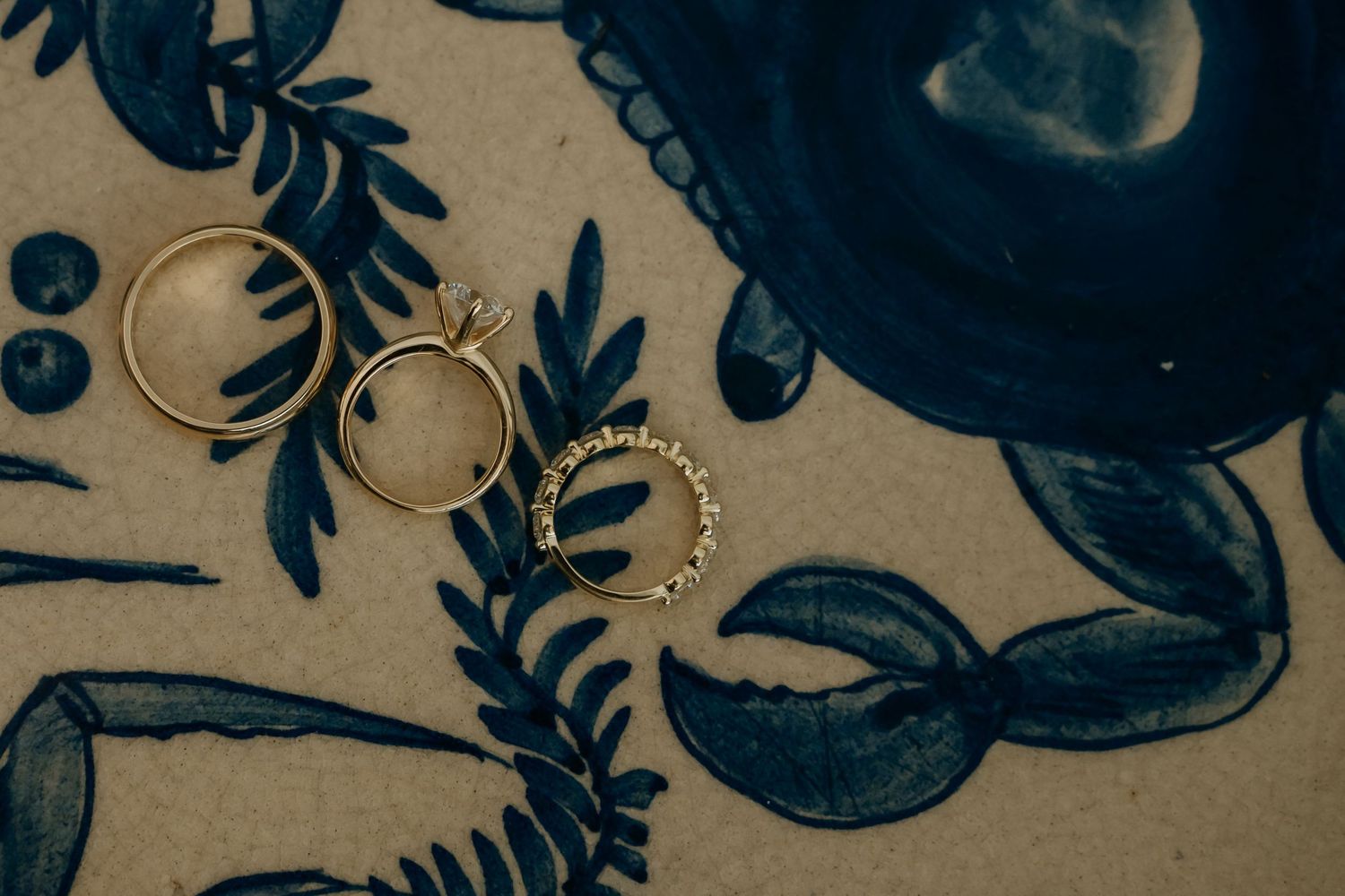 Two gold wedding rings with diamonds displayed on a decorative blue floral patterned fabric surface.