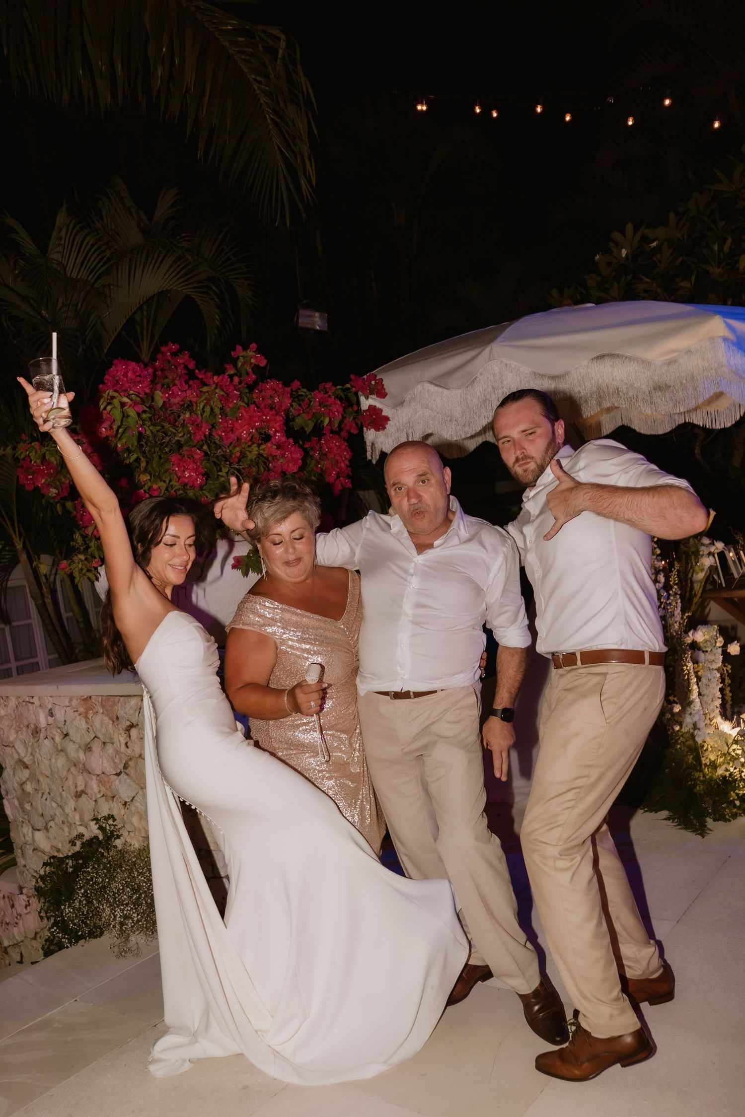 Bride and groom celebrate with family on wedding dance floor surrounded by tropical florals.