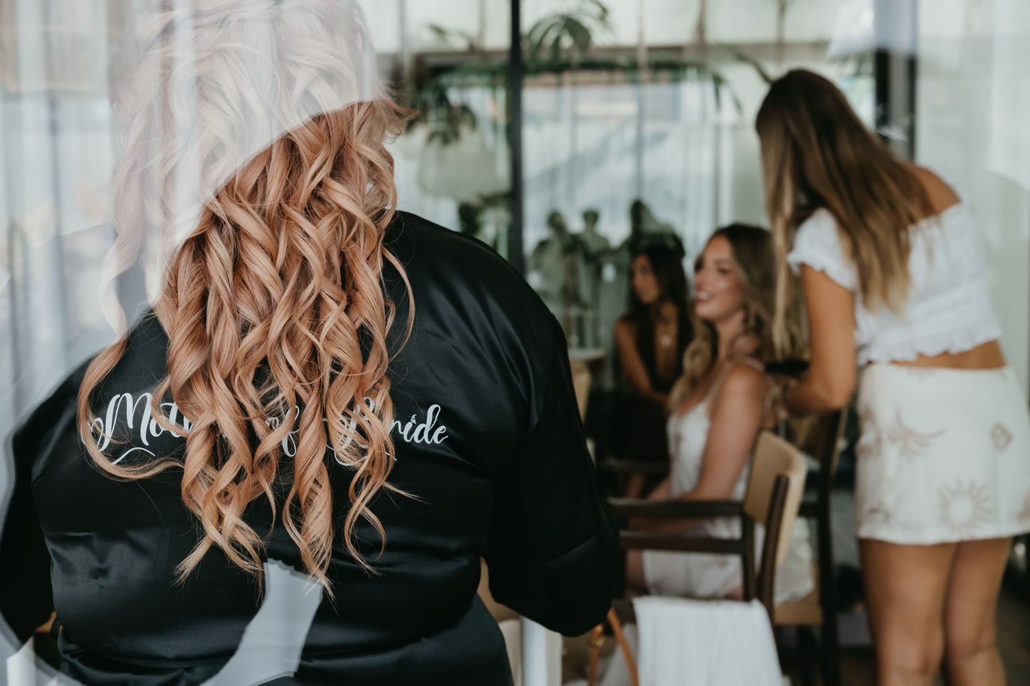 Bride's mother in black satin robe with curly blonde hair during wedding preparations with bridesmaids.
