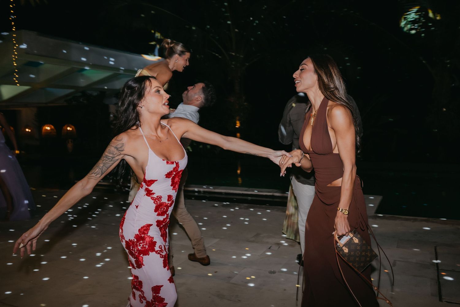 Two women in elegant dresses dancing together at an outdoor wedding reception at night.