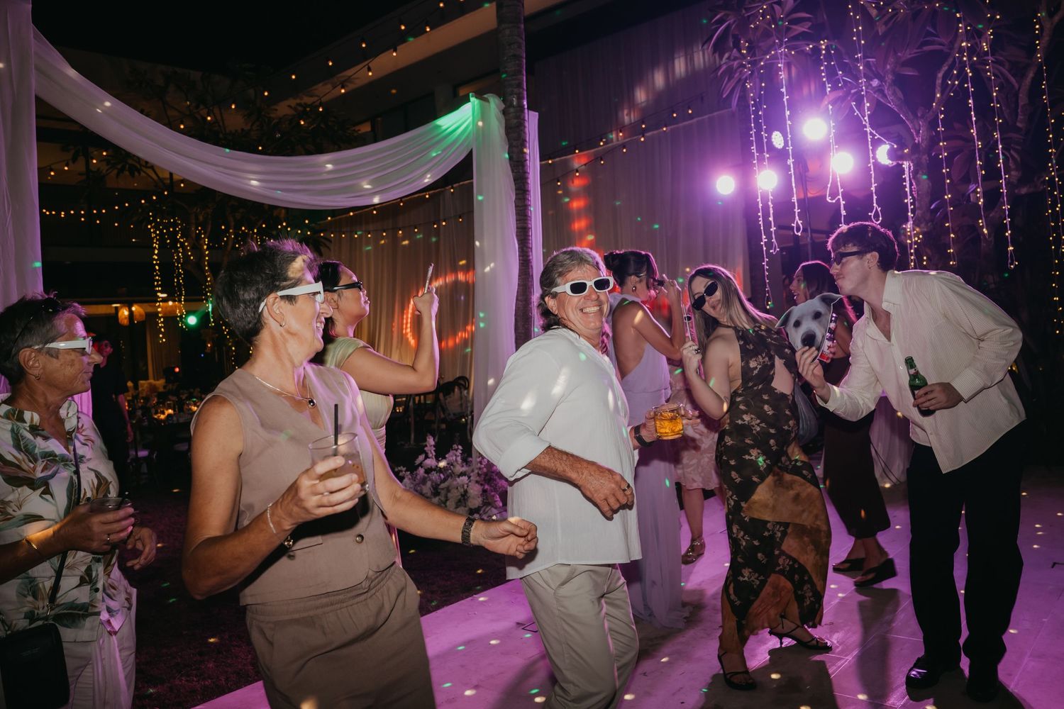 Guests dancing under colorful lights at an outdoor wedding reception at night.